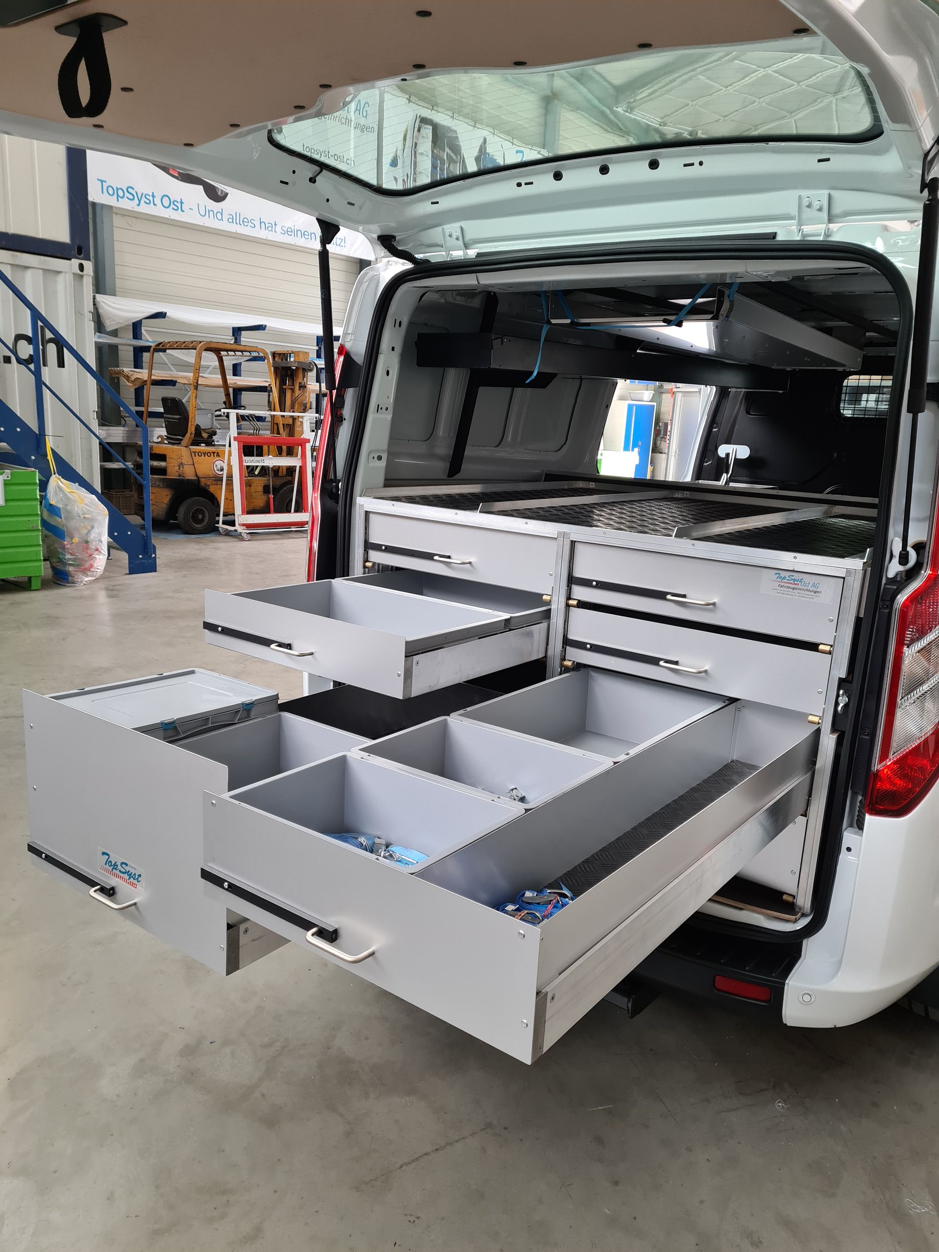 Weißer Lieferwagen mit offenem Heck und individuell gestalteten Schubladen im Freien.