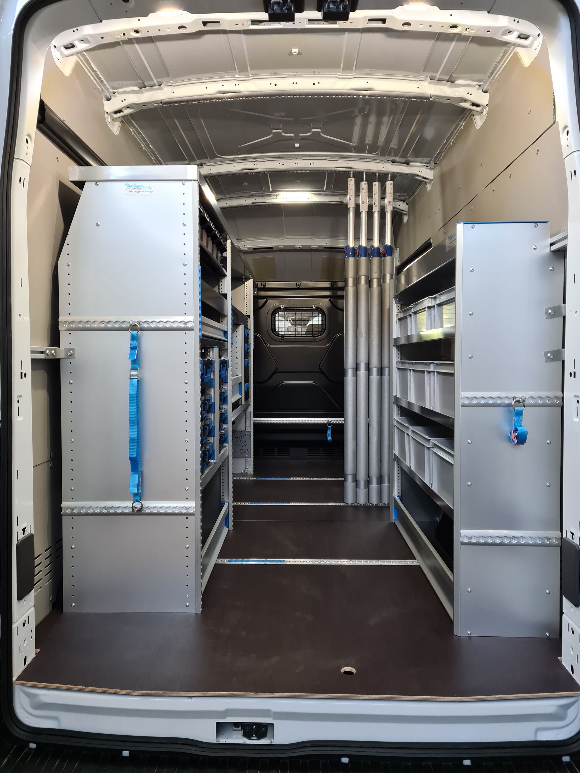 Innenraum eines weißen Lieferwagens mit Metallregalen, Lagerbehältern und Werkzeugen, organisiert für einen Handwerker.