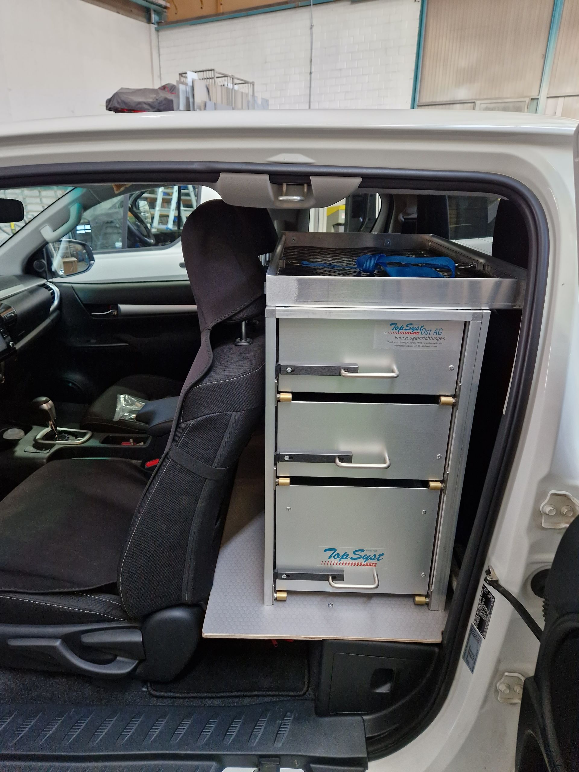 Silbernes Aufbewahrungsmöbel mit Schubladen, eingebaut im Rücksitzbereich eines weißen Trucks.