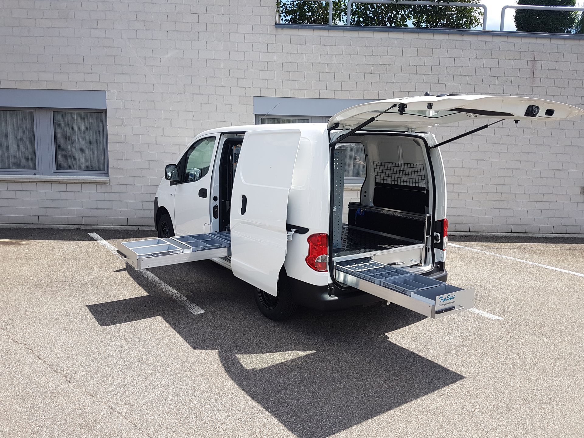 Weißer Lieferwagen mit offenen Türen und ausziehbaren Rampen auf einem Parkplatz.