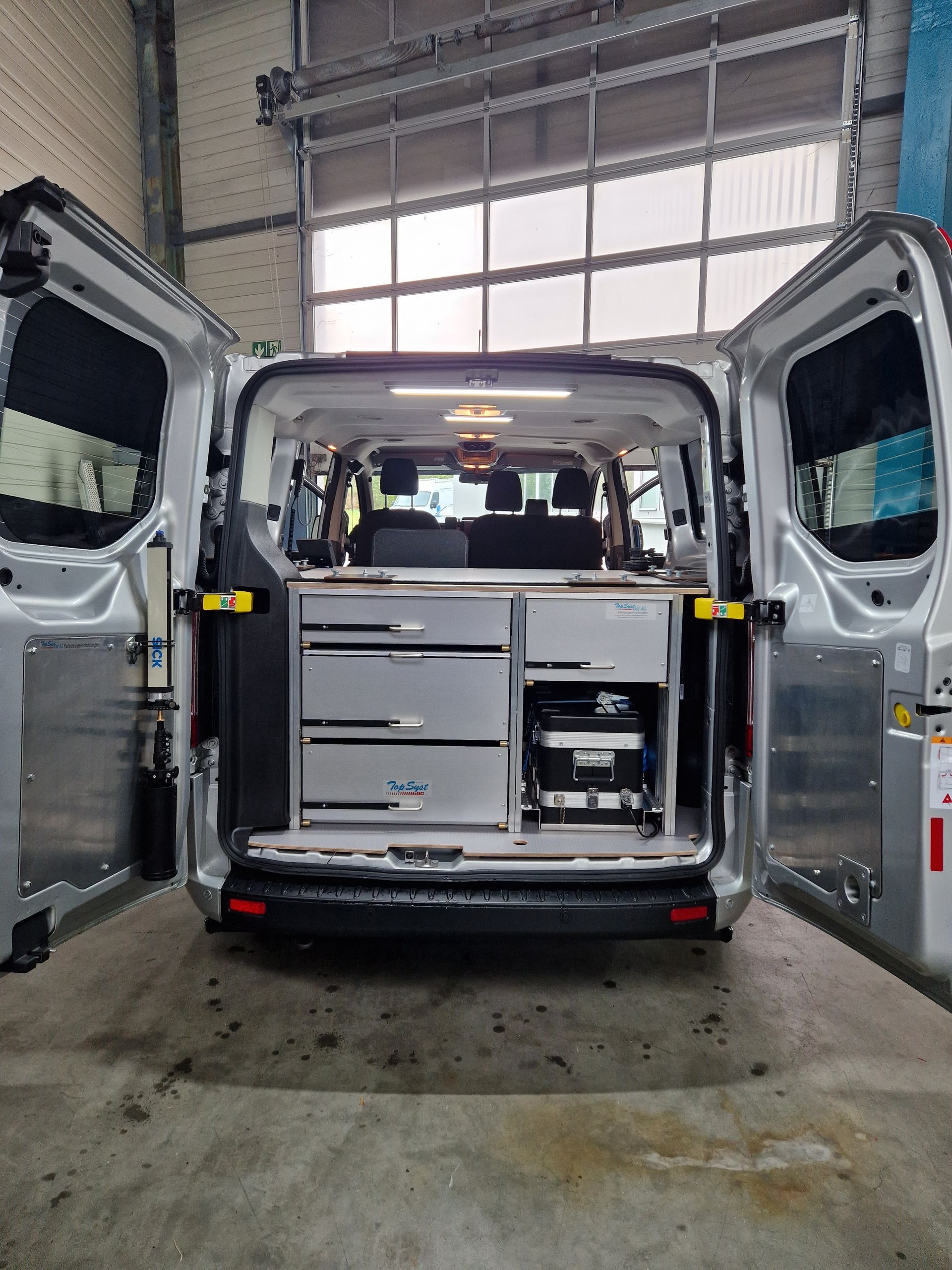 Silberner Van-Innenraum mit offenen Türen, maßgefertigten Schränken, von hinten gesehen, Innenansicht.