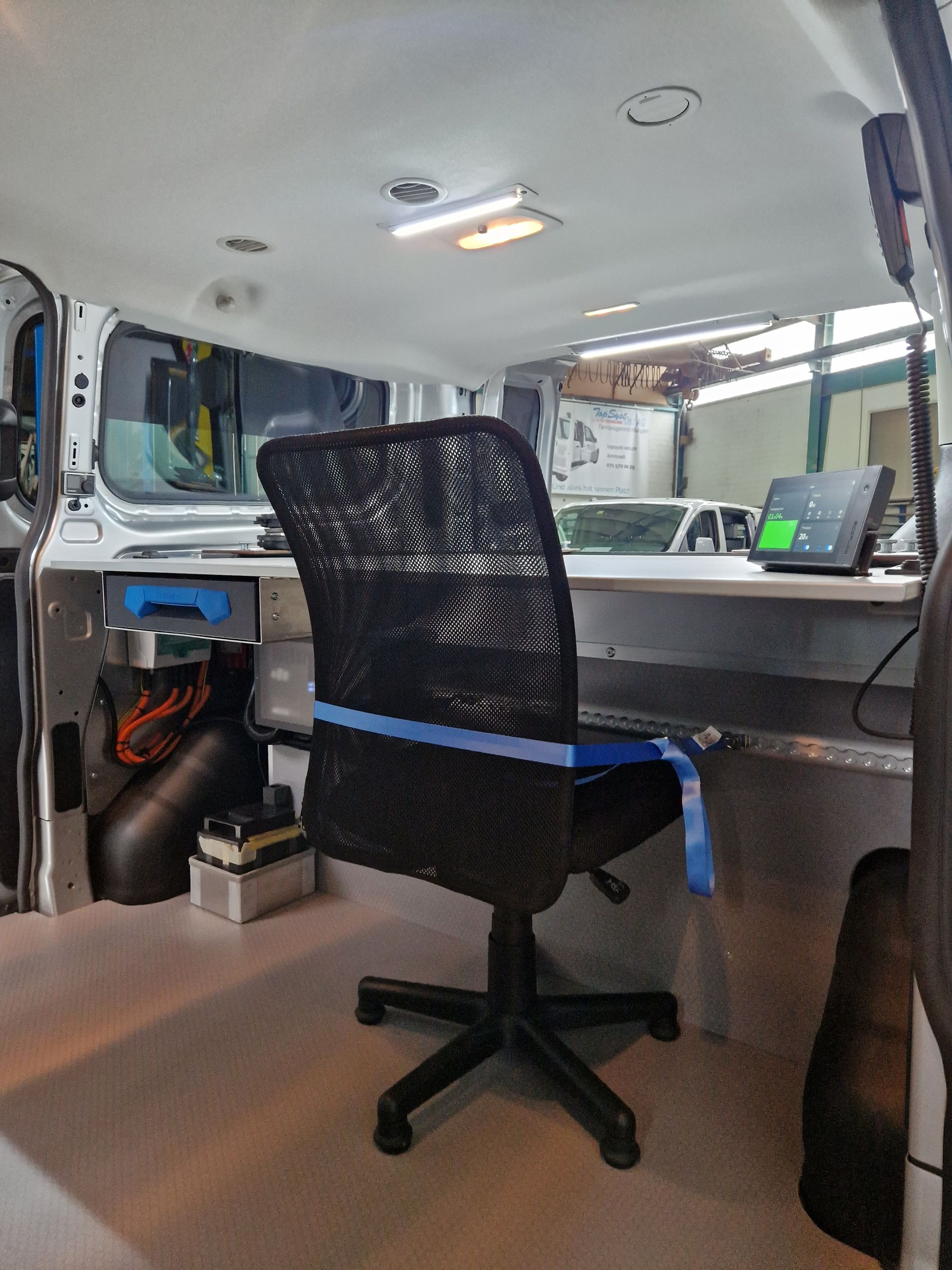 Innenraum eines in ein mobiles Büro umgebauten Lieferwagens; inklusive Schreibtisch, Stuhl und Ausrüstung.