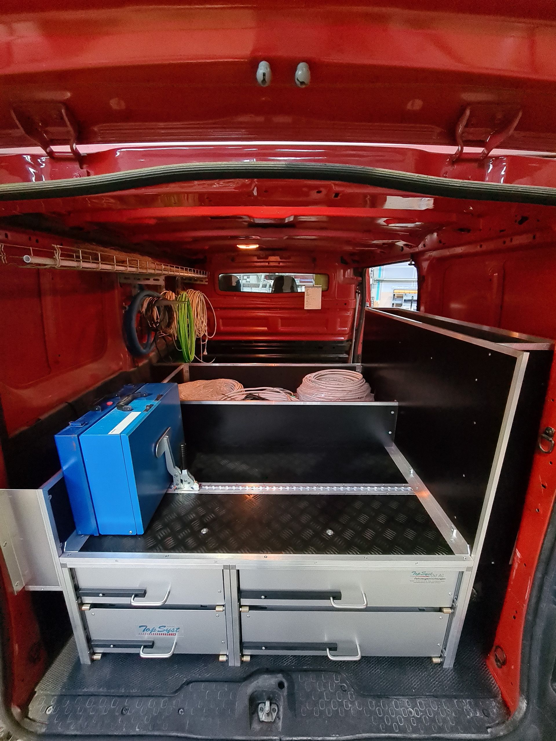 Innenraum eines roten Lieferwagens, individuell gebaut mit Schubladen, Regalen und Werkzeugaufbewahrung.
