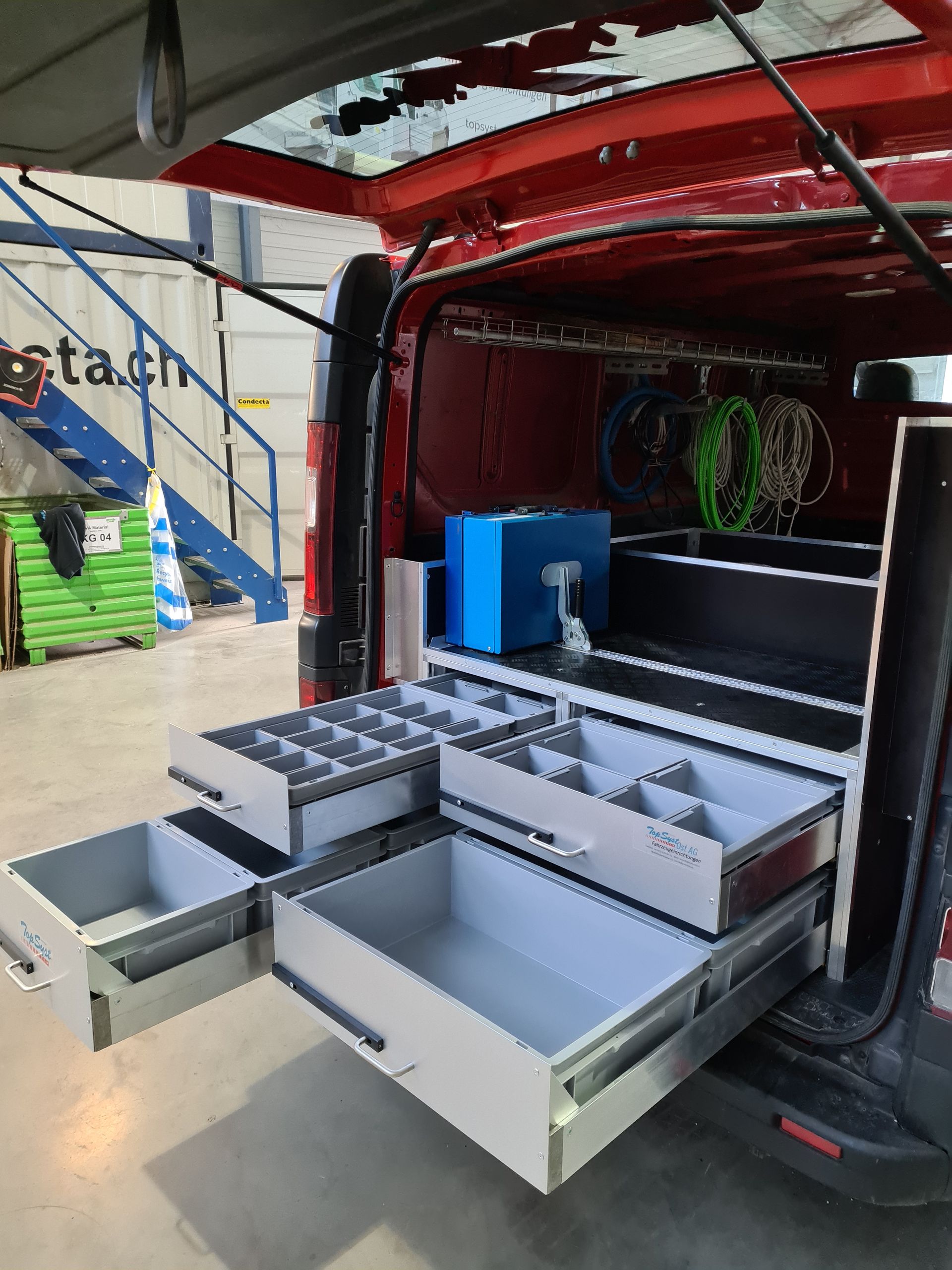 Innenraum eines roten Lieferwagens mit offenen grauen Schubladen voller Werkzeuge.