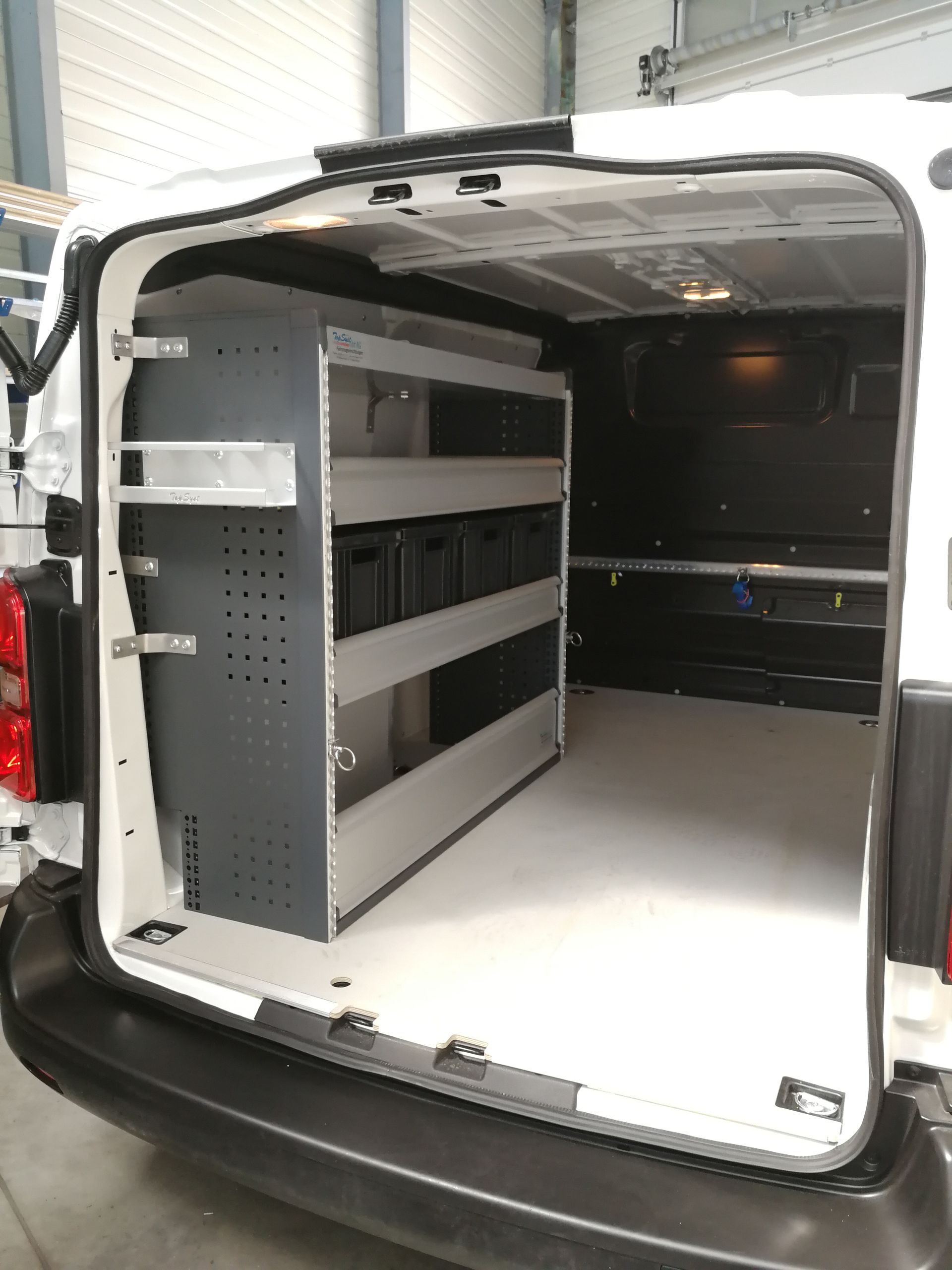Innenraum eines weißen Lieferwagens mit Regalen und Lagerbehältern auf einer Seite. Leerer Laderaum.