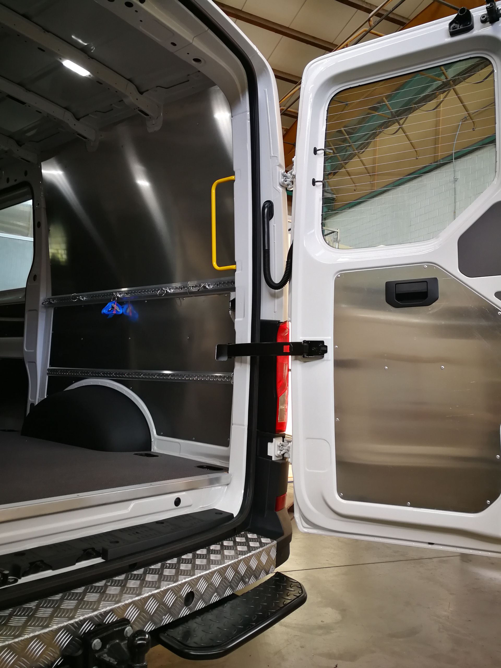 Offene weiße Lieferwagentür, Innenausstattung und Trittstufe aus Aluminium zu sehen, im Innenbereich geparkt.