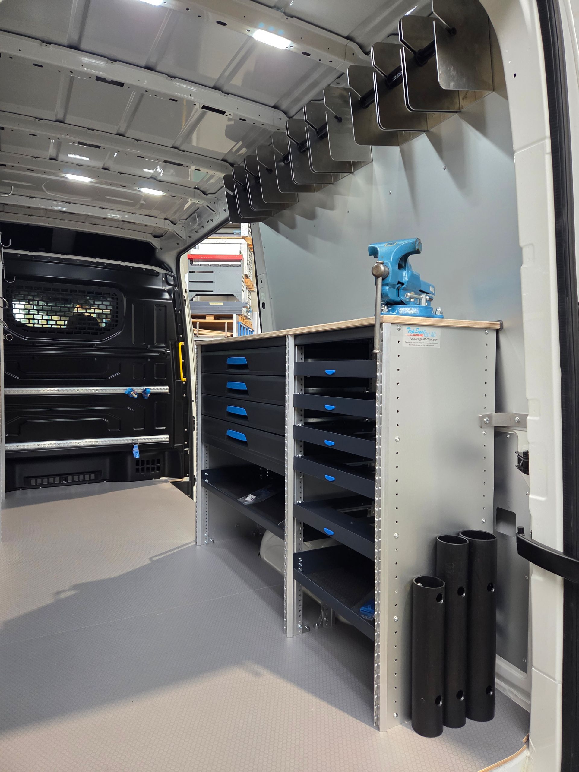 Innenraum eines Arbeitswagens mit Werkzeugschränken, einem montierten Schraubstock und verschiedenen Werkzeugen für Reparaturen vor Ort.