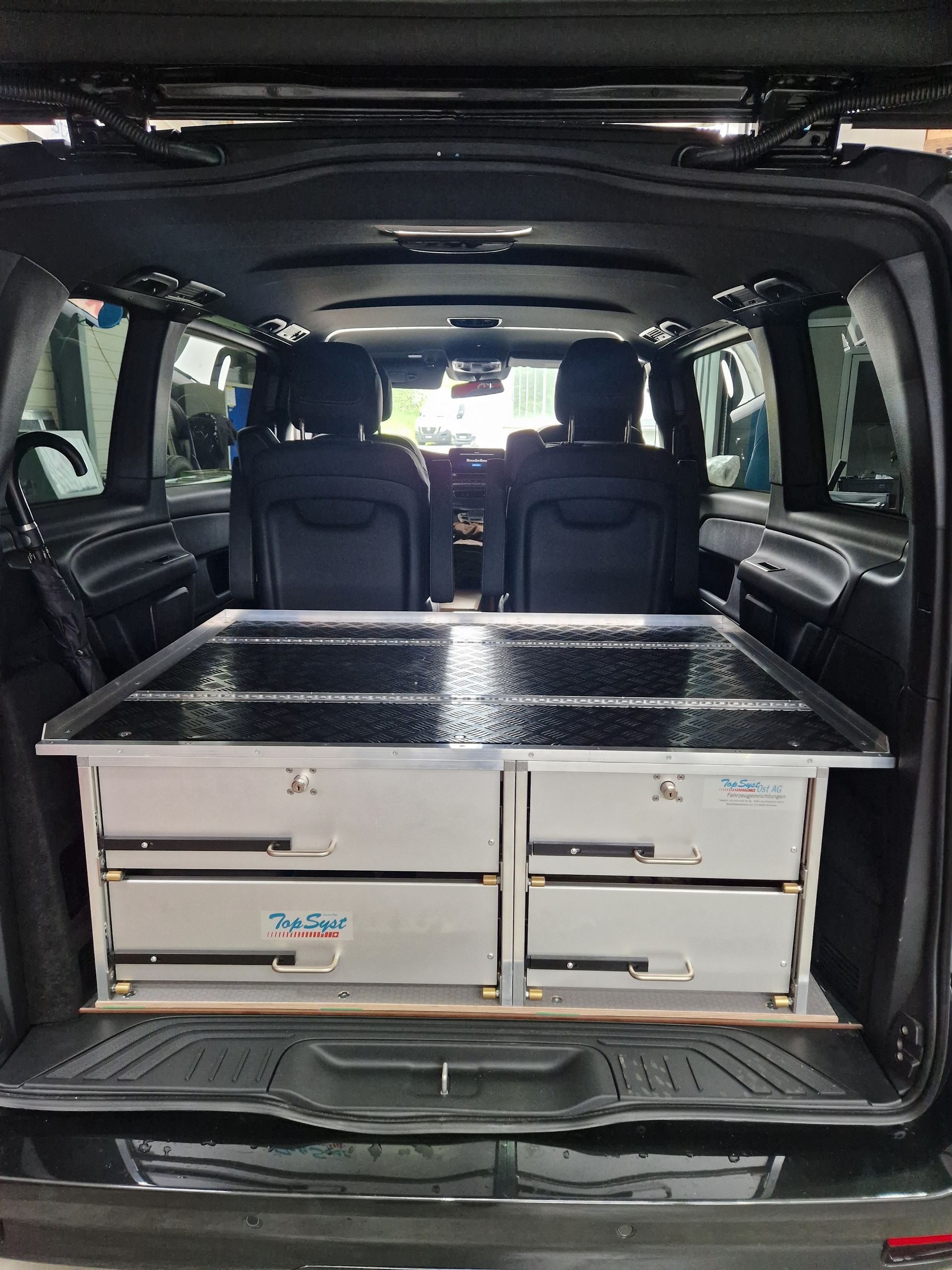 Schwarzer Van-Innenraum mit eingebauten Schubladen und Sitzen.