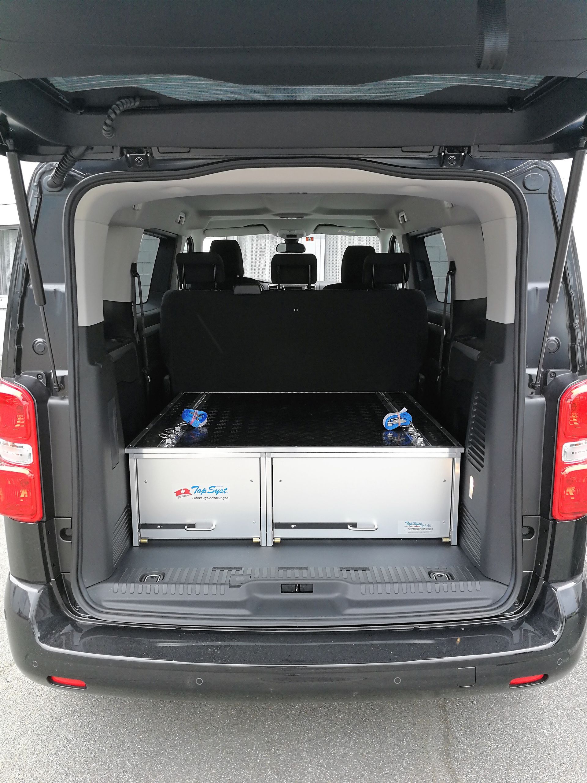 Schwarzer Lieferwagen mit offener Rückseite, die im Inneren einen Metallschrank freigibt.