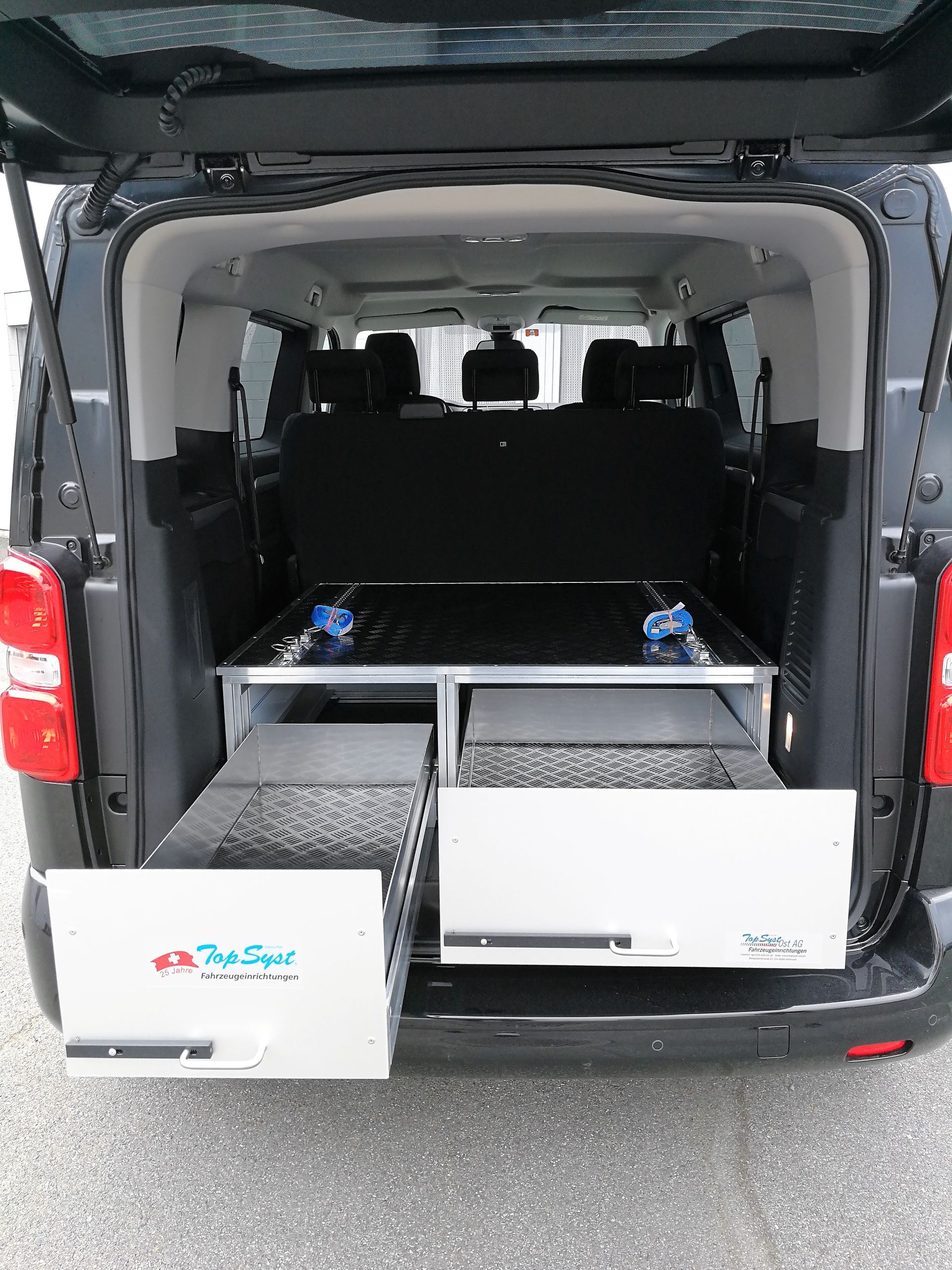 Das offene Heck des dunklen Lieferwagens gibt den Blick auf Schubladen frei; Aufbewahrungseinheit mit blauen Knöpfen. Weiße und graue Schubladen sichtbar.