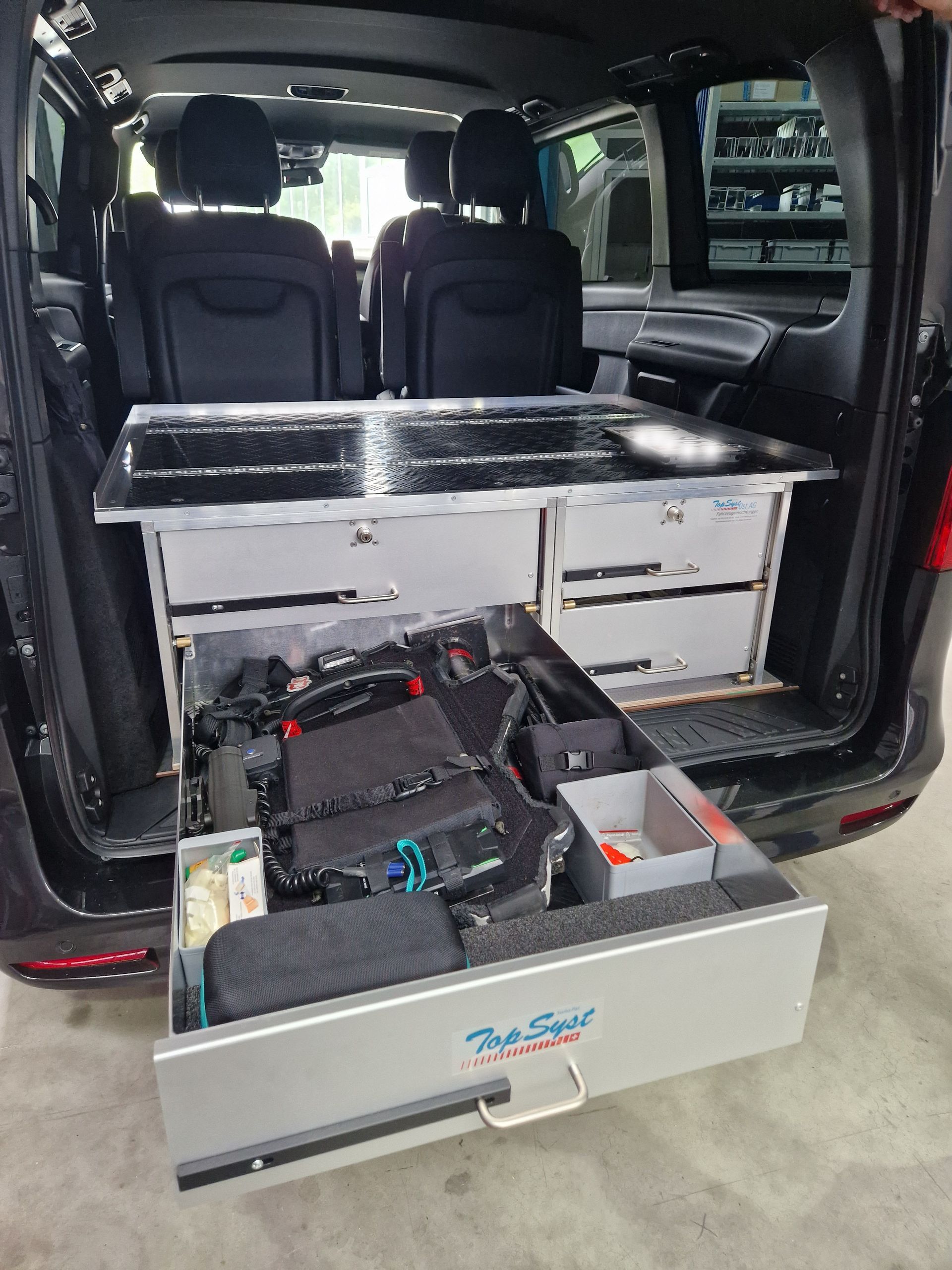 Ein rollstuhlgerechter Van-Innenraum mit Schubladen und Tisch. Die Hecktür ist geöffnet.