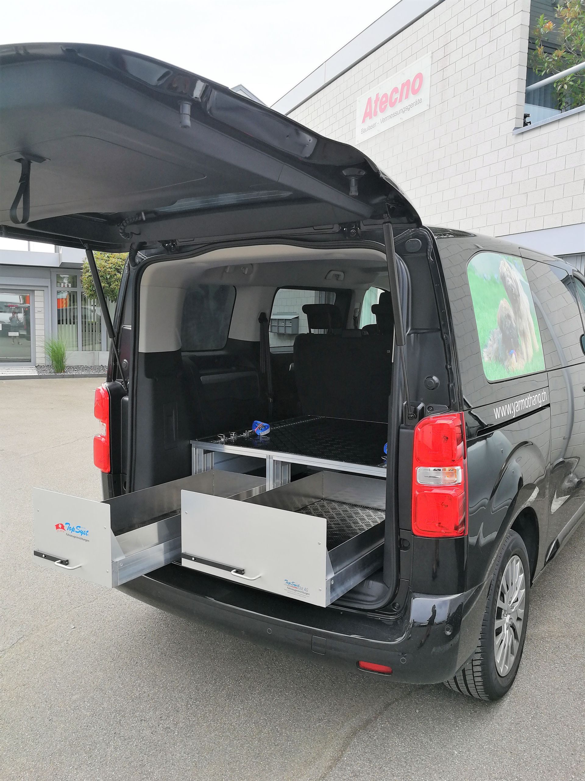 Schwarzer Lieferwagen mit geöffneter Hecktür, hinter der sich ausziehbare Schubladen befinden.