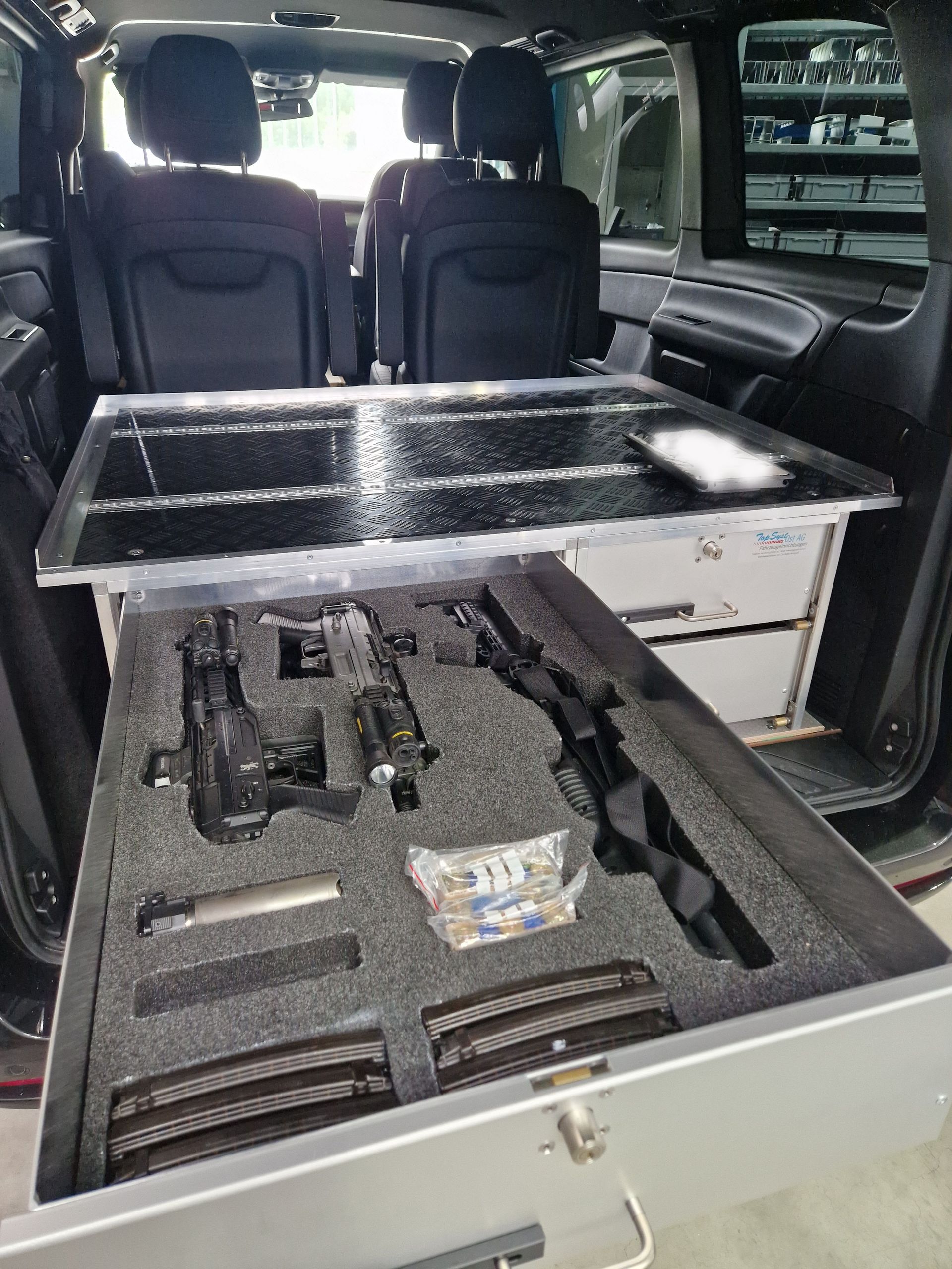 Eine Schublade mit Schusswaffen und Munition im Inneren eines Fahrzeugs, von hinten betrachtet.