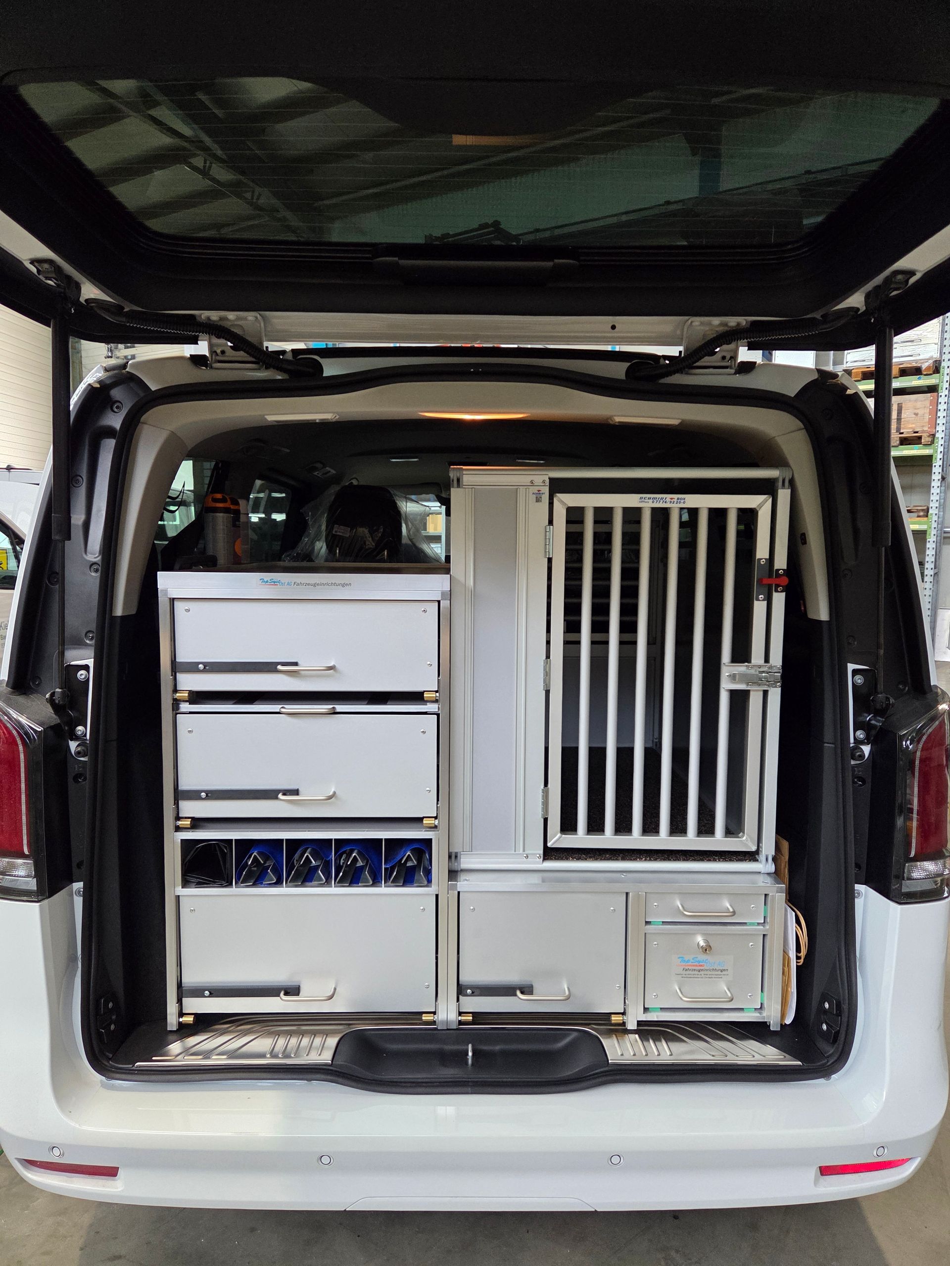 Für Hunde umgebauter Innenraum eines weißen Lieferwagens mit Schubladen und einer Hundehütte.