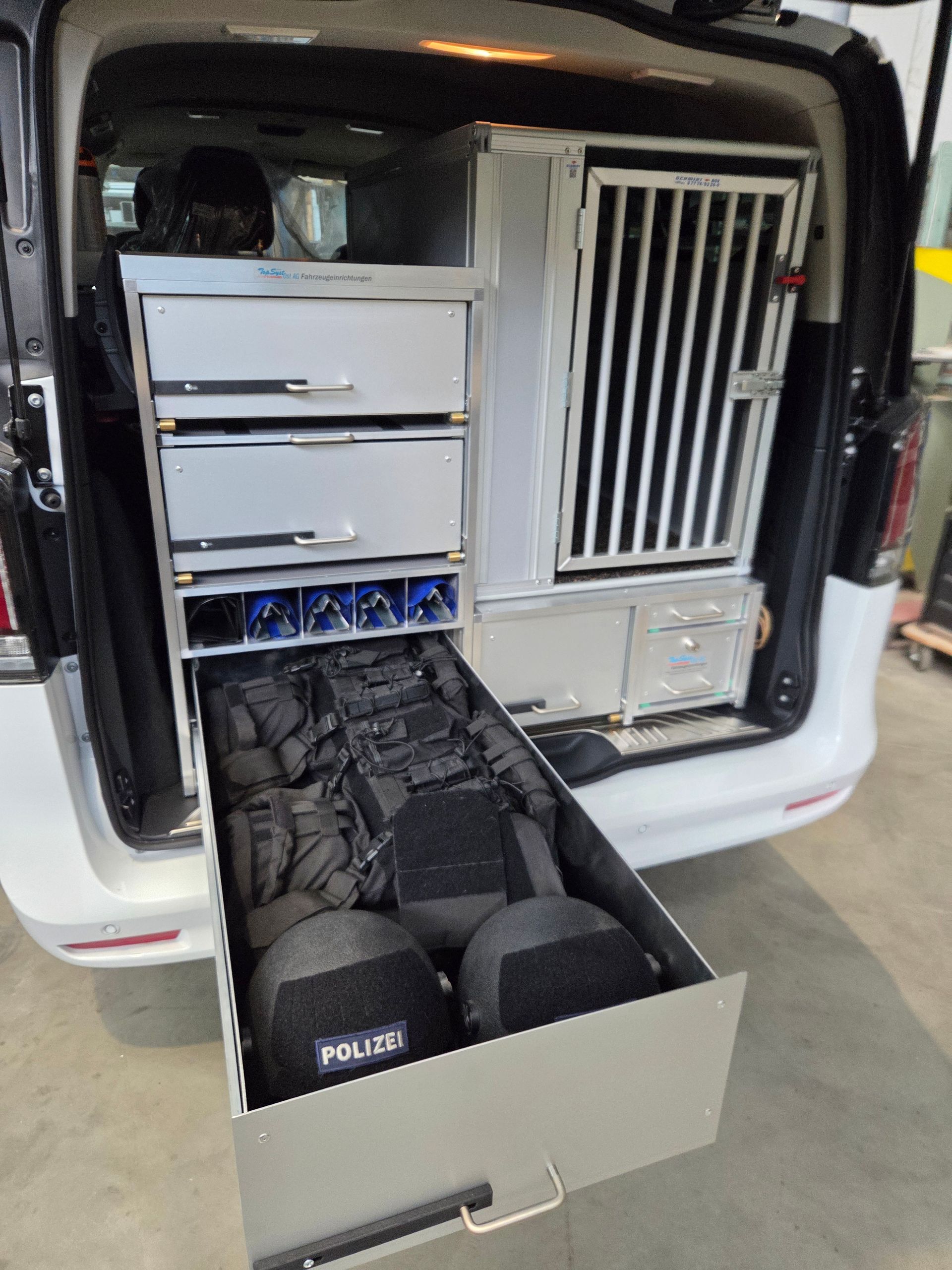 Innenraum eines Lieferwagens mit offenen Schubladen, die Ausrüstung enthalten, darunter Körperpanzerung und ein Käfig.