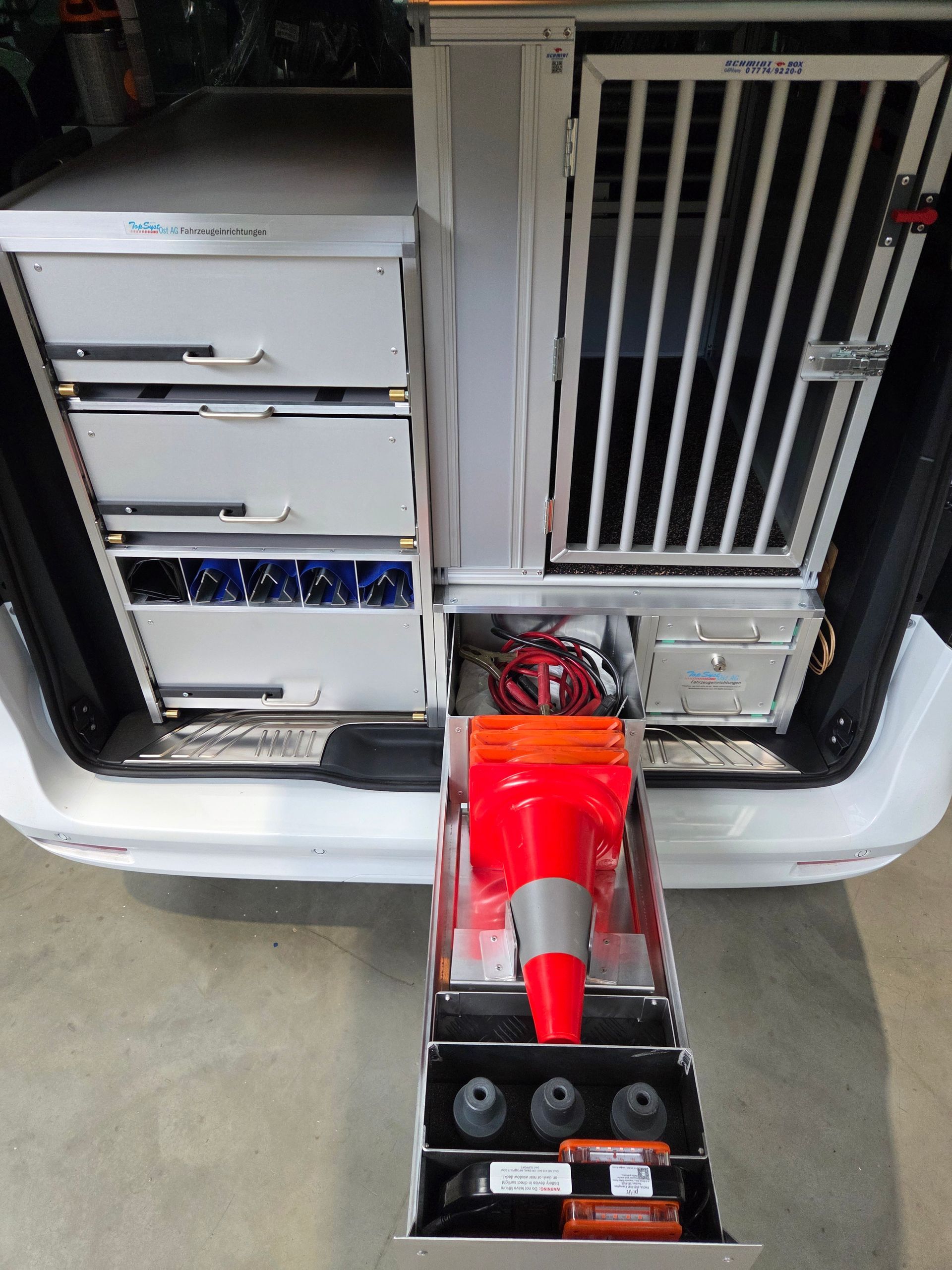 Rückseite eines weißen Fahrzeugs mit Stauraum, einschließlich Schubladen, Sicherheitskegeln und einem abgesperrten Fach.