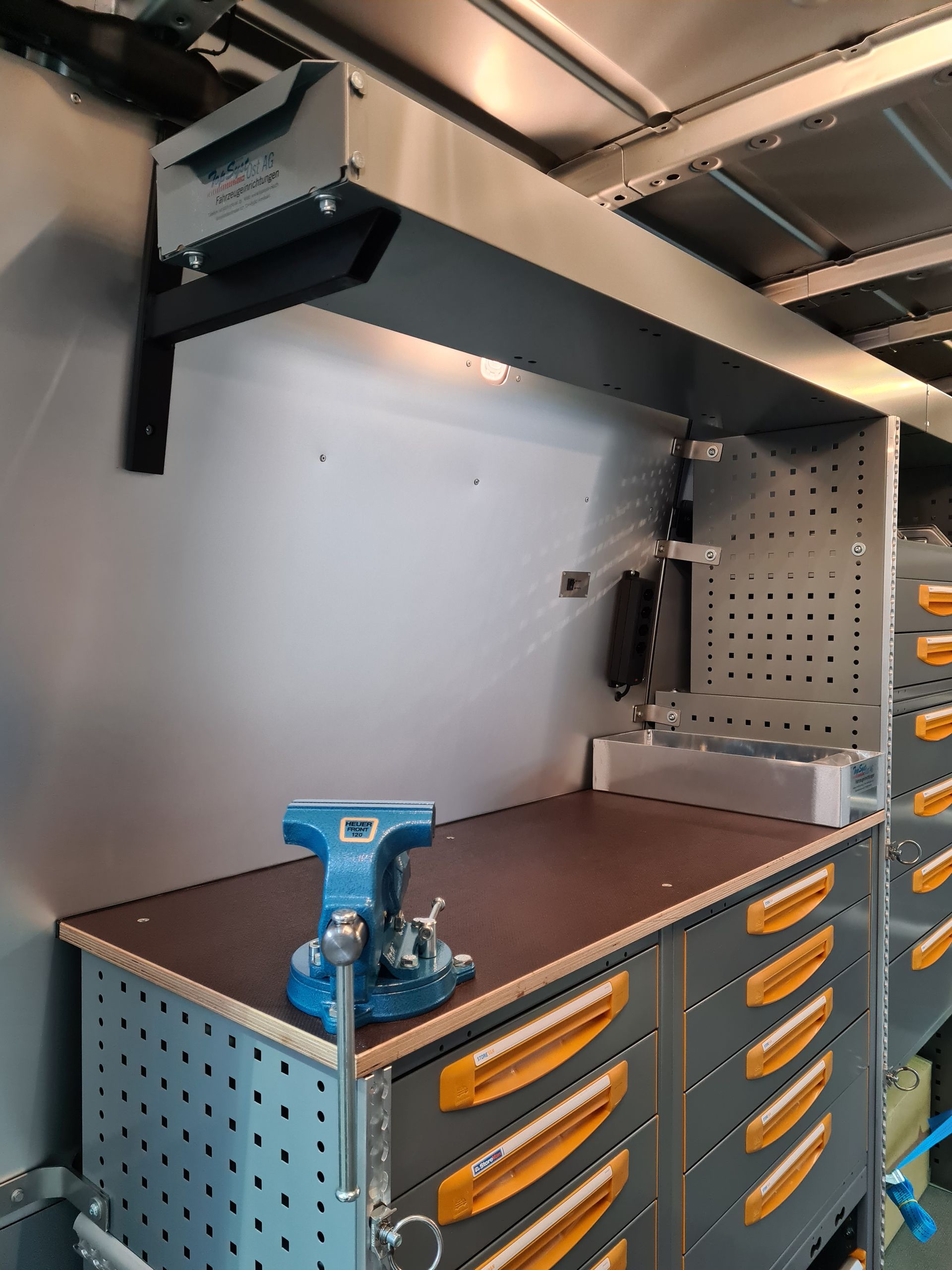 Werkstattinnenraum mit Werkbank, Schraubstock, Werkzeugschubladen und Deckenbeleuchtung.