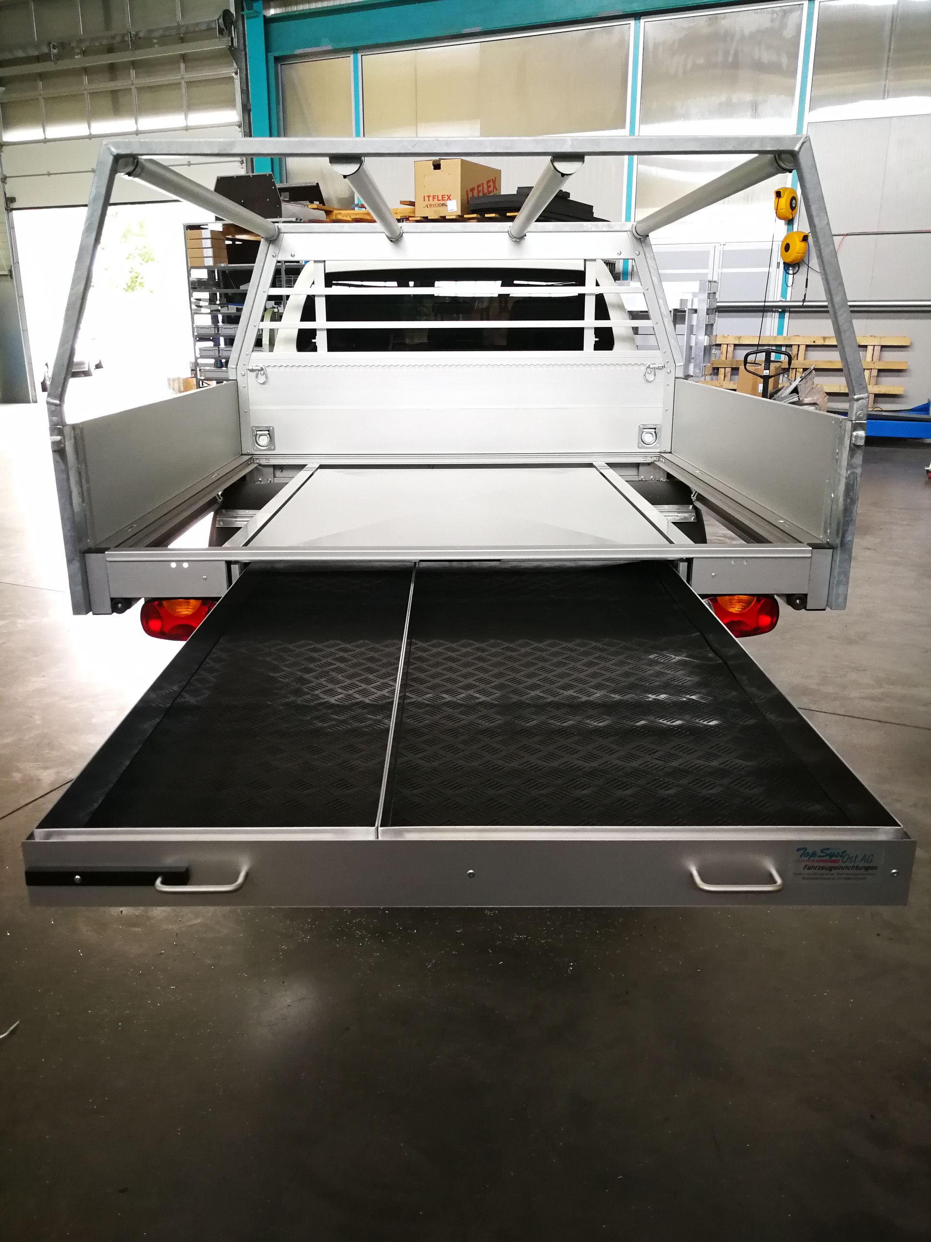 Graue Ladefläche mit ausziehbarer Schublade in Fabrikeinstellung, Heckklappe heruntergeklappt.