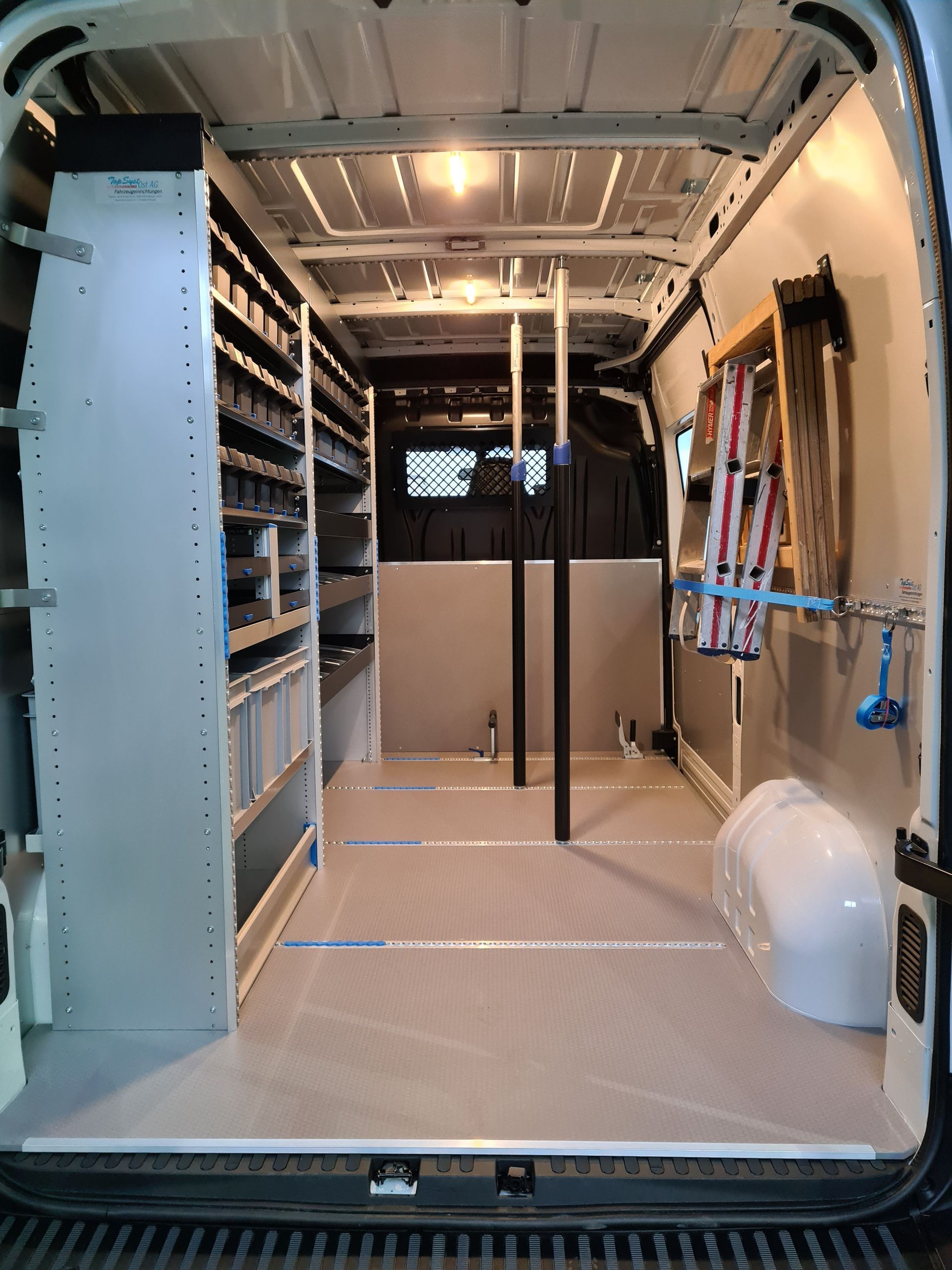 Innenansicht eines weißen Arbeitstransporters mit Regalen, Lagerräumen und an den Wänden montierten Werkzeugen, bereit für die Arbeit.
