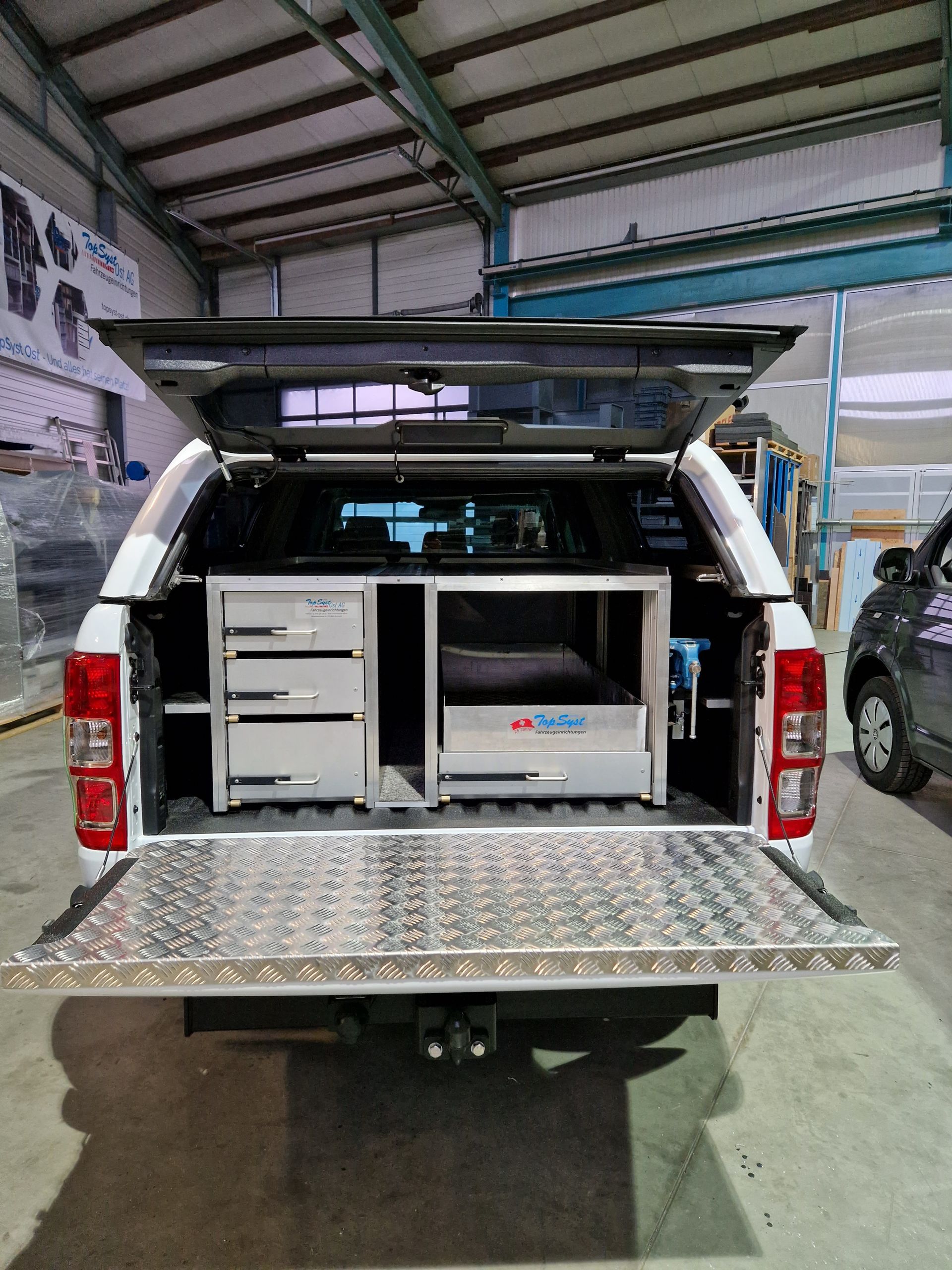 Weiße Ladefläche mit offenem Verdeck, das Schubladen und Arbeitsbereich freigibt.