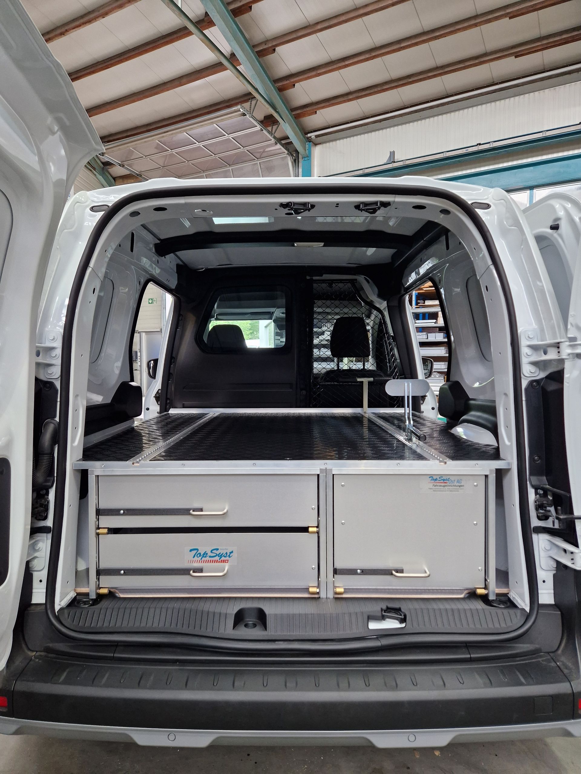 Innenraum eines weißen Lieferwagens, ausgestattet mit Metallschubladen und Regalen zur Aufbewahrung.