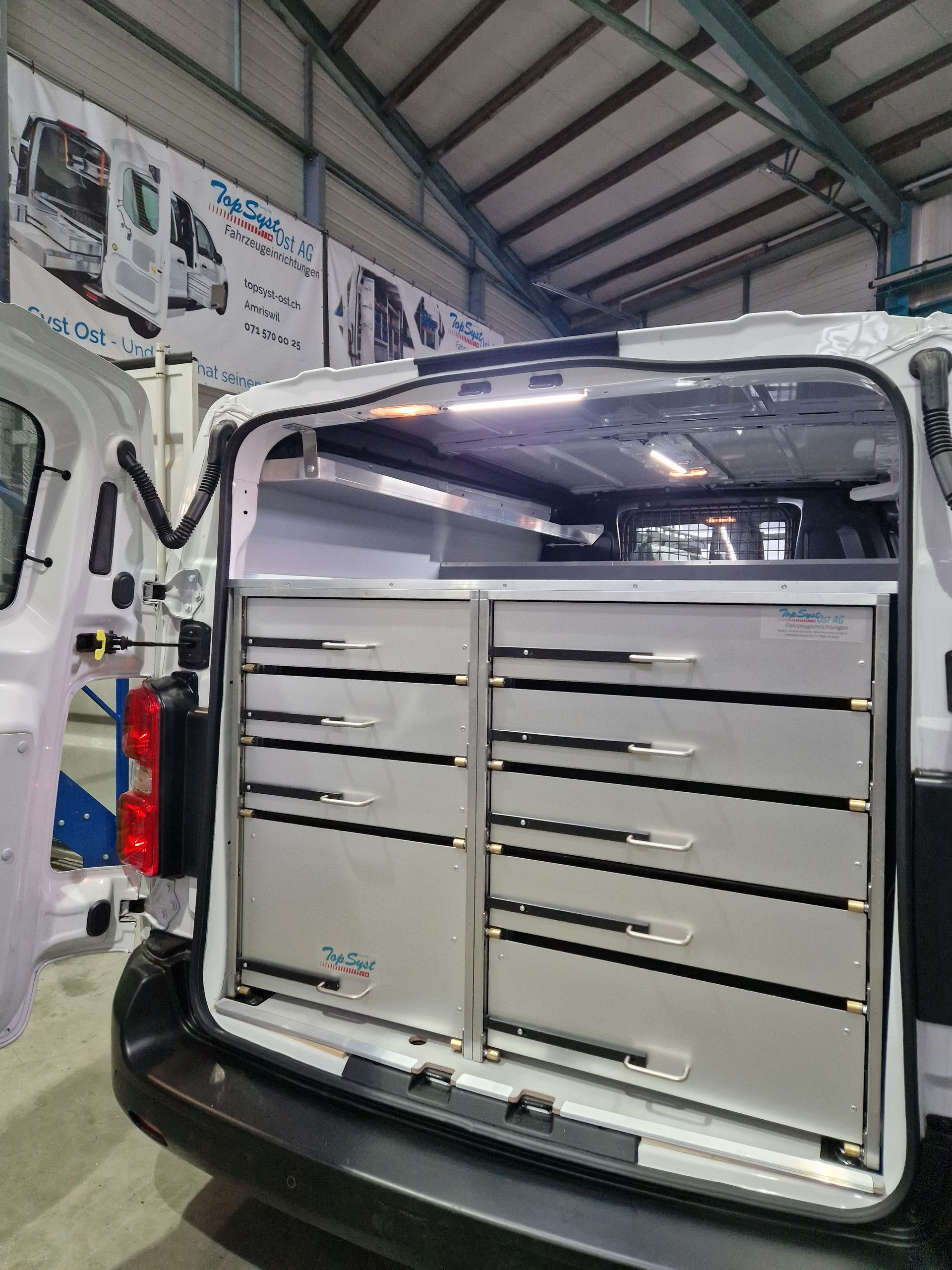 Die offene Ladefläche eines weißen Lieferwagens gibt den Blick auf silberne Schubladen und Stauraum frei. Im Inneren eines Lagerhauses.