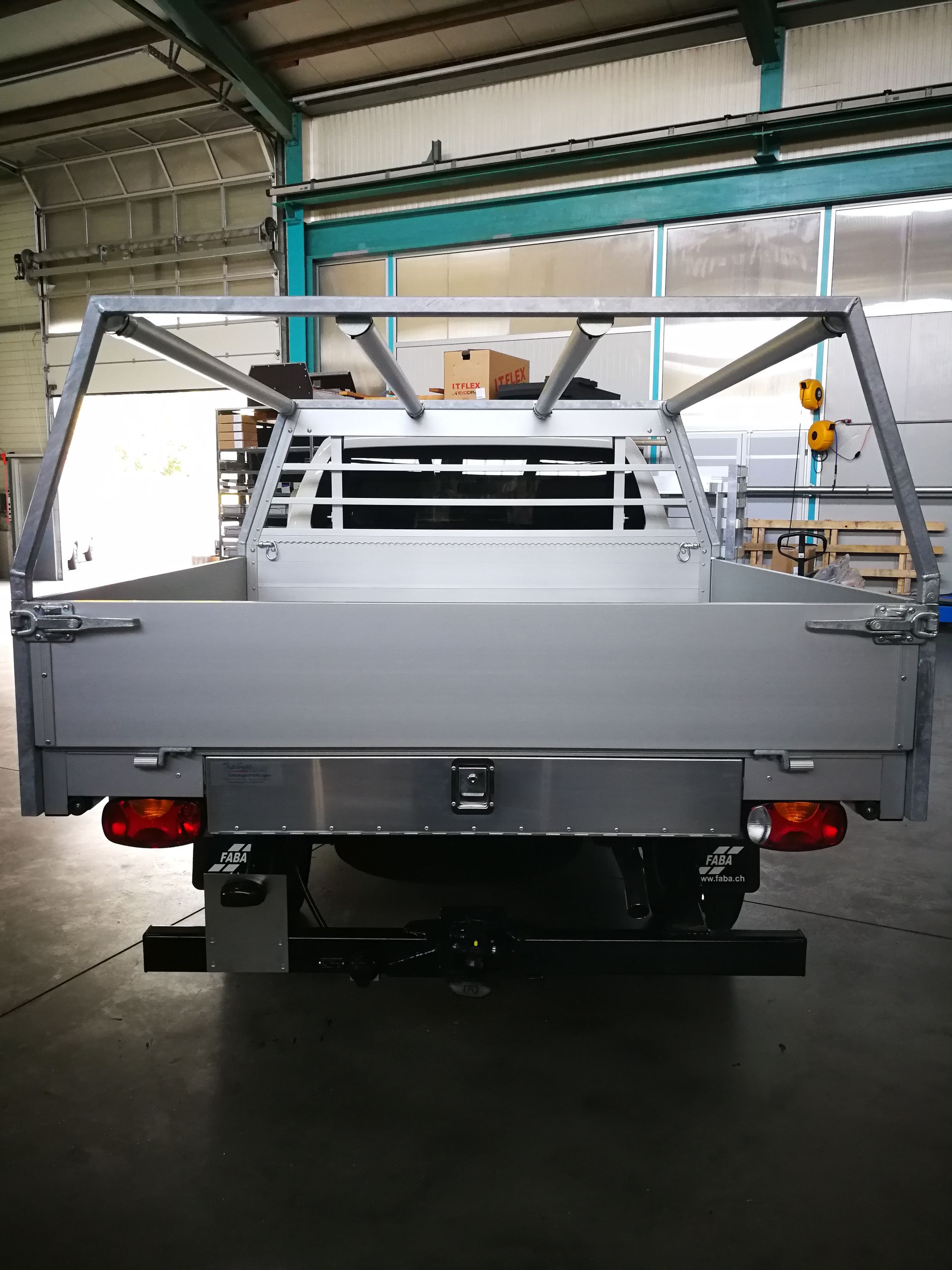 Rückansicht einer silbernen Ladefläche eines Nutzfahrzeugs mit Metallrahmen und Aufbewahrungsbox in einem Lagerhaus.