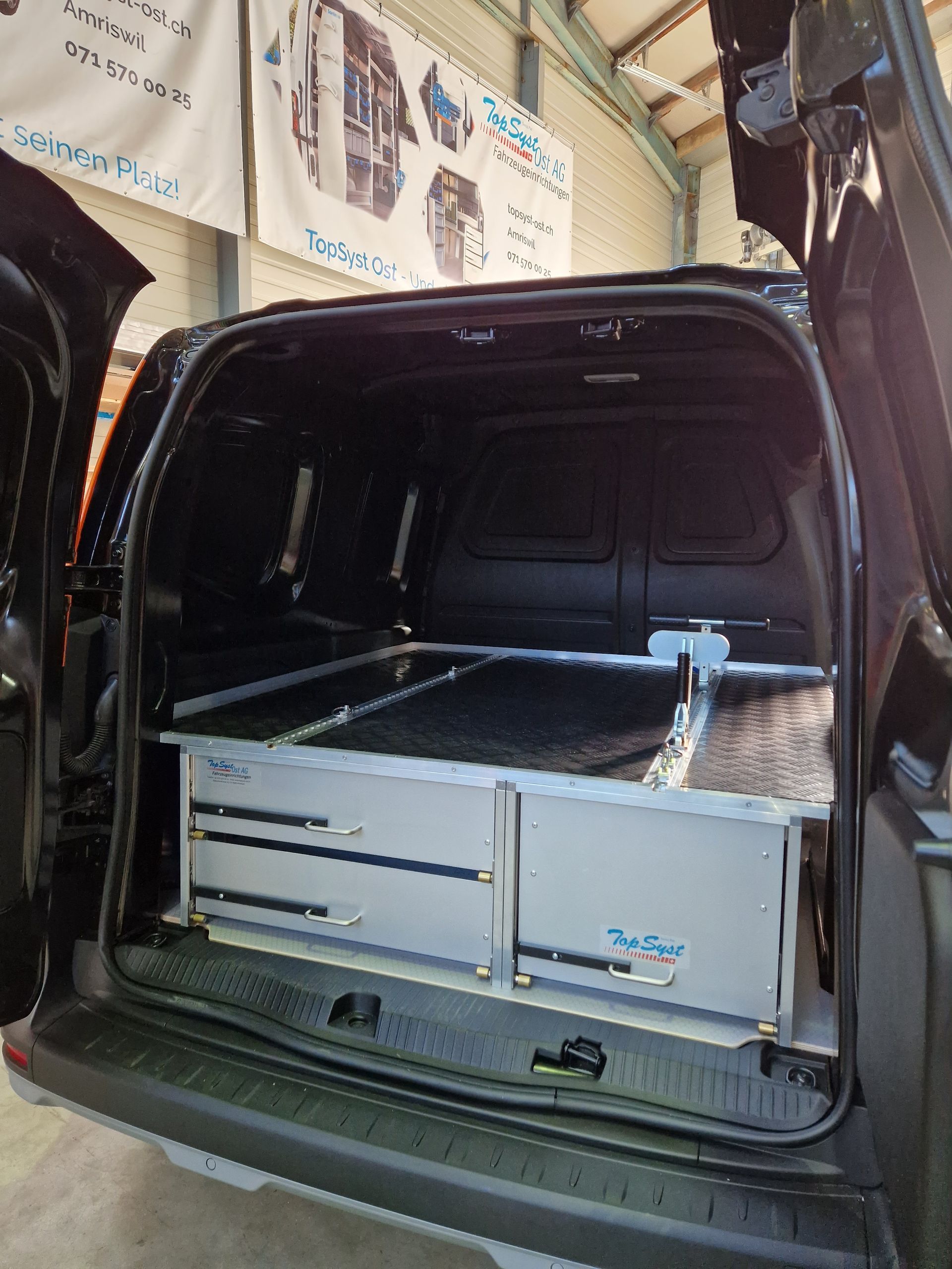 Schwarzer Van-Innenraum mit silbernen Schubladen und Regalen. Offene Türen.