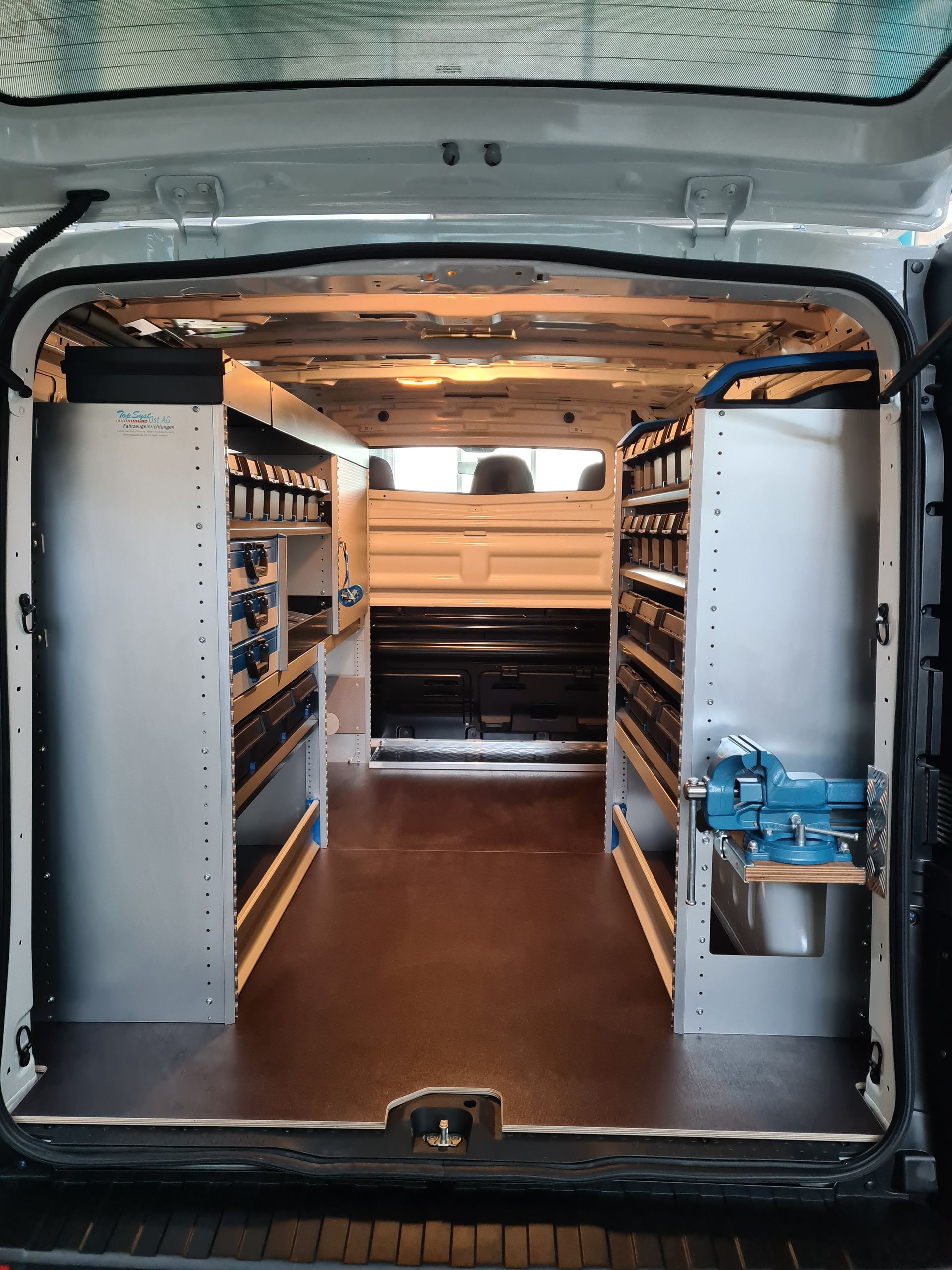 Innenraum eines Arbeitstransporters mit Lagerregalen auf beiden Seiten und sichtbaren Werkzeugen.
