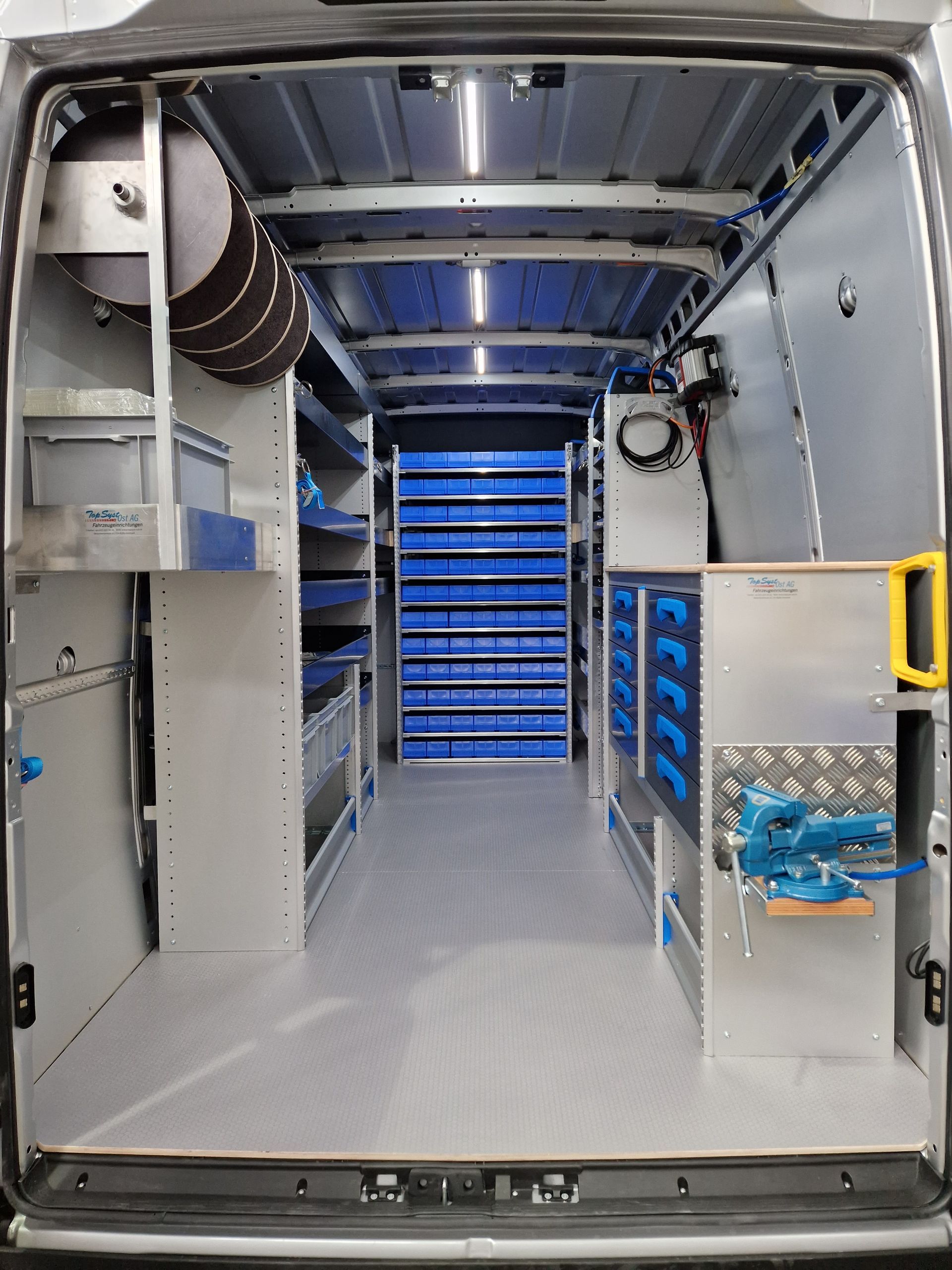 Innenraum eines Arbeitstransporters, gut organisiert mit Regalen, Schubladen und Werkzeugen. Farbschema in Grau und Blau.