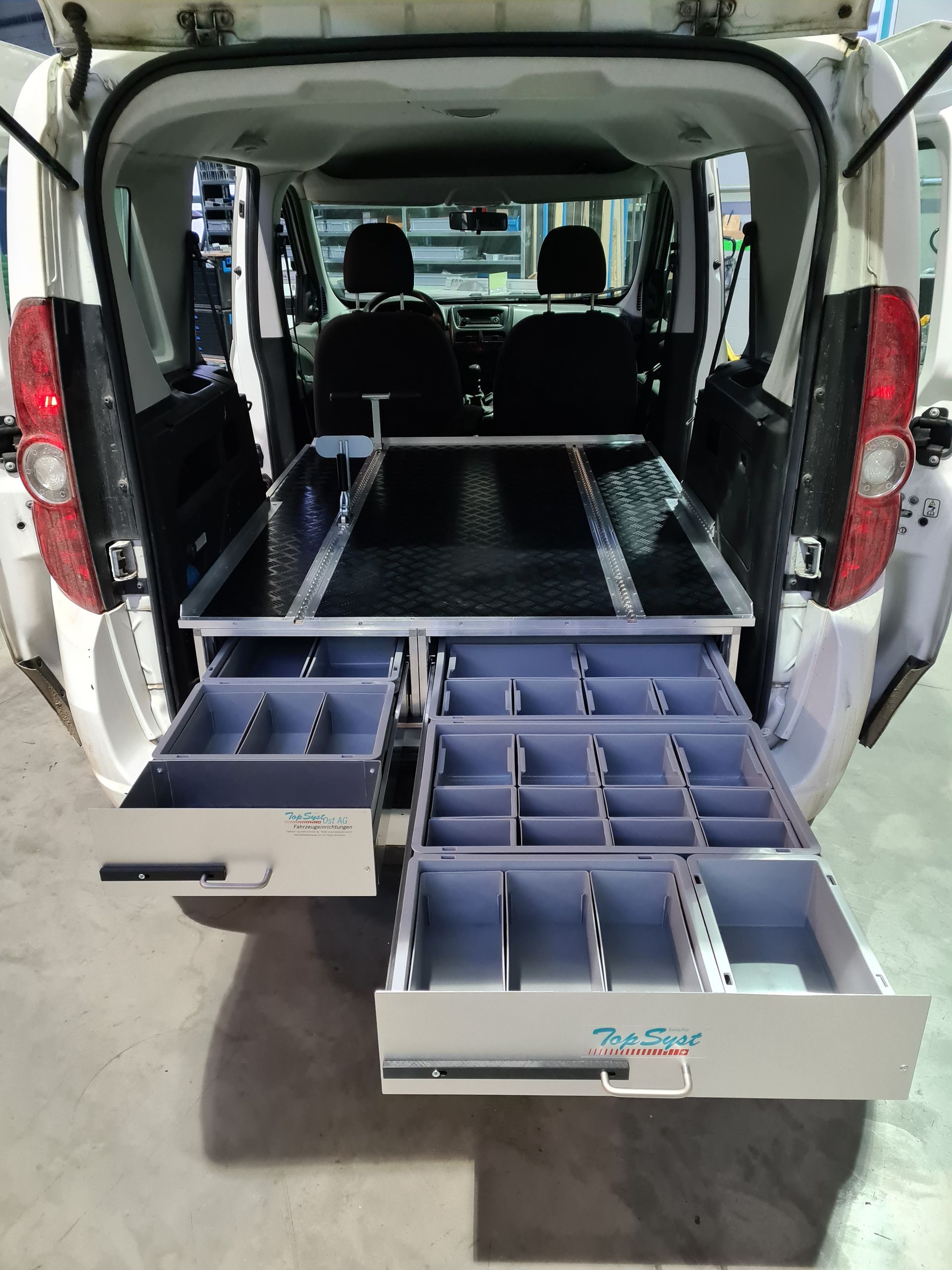 Weißer Van-Innenraum mit ausziehbaren Schubladen für Werkzeuge und Ausrüstung, offen, organisiert und einsatzbereit.