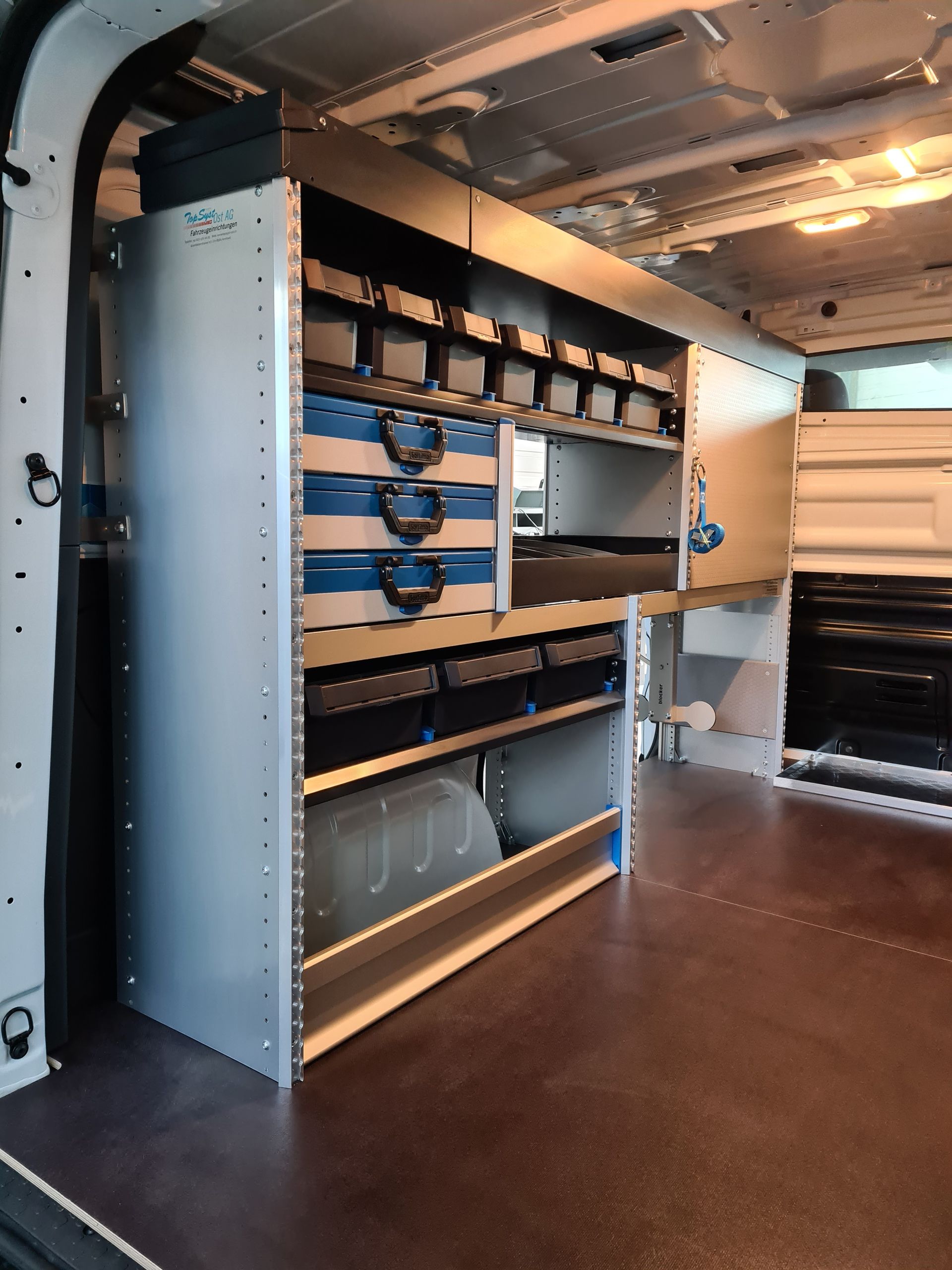 Innenansicht eines Lieferwagens mit eingebauten Regalen und Lagerbehältern für Werkzeuge und Ausrüstung.
