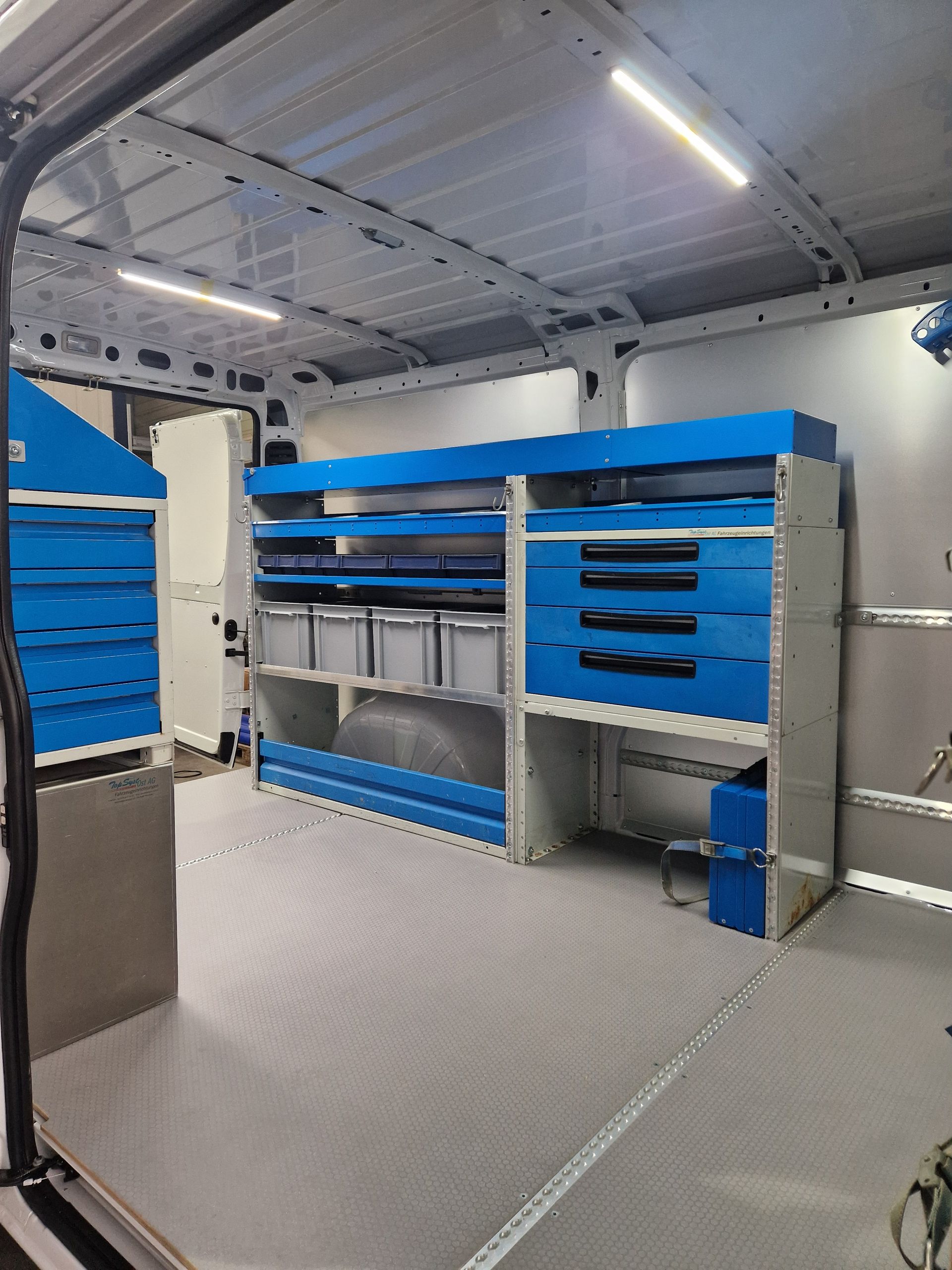 Innenansicht eines Servicewagens mit blauen Lagerschränken und Schubladen auf grauem Boden.