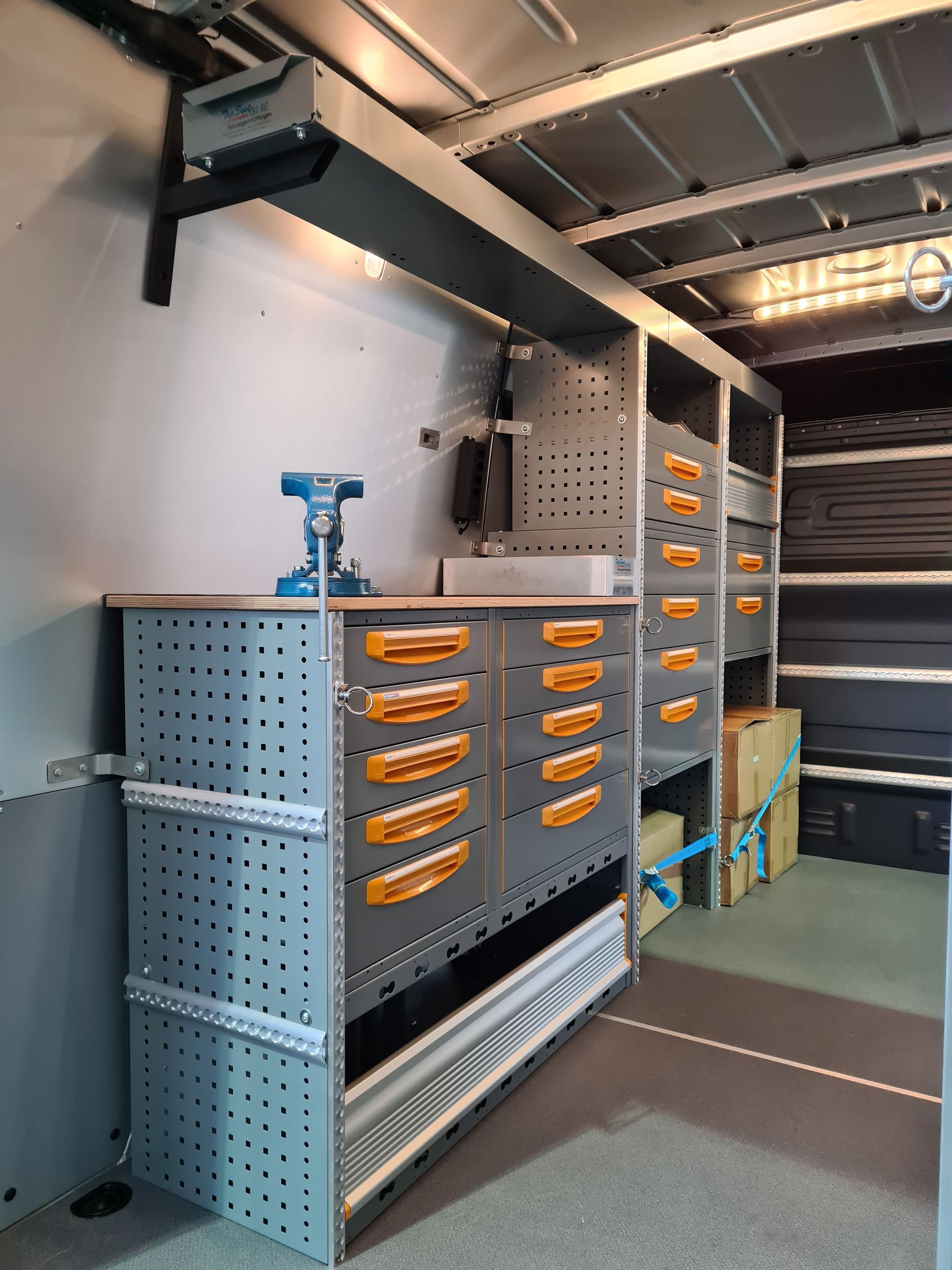 Innenraum eines Lieferwagens mit grauen Regalen und Schubladen, Werkzeugen und Stauraum.