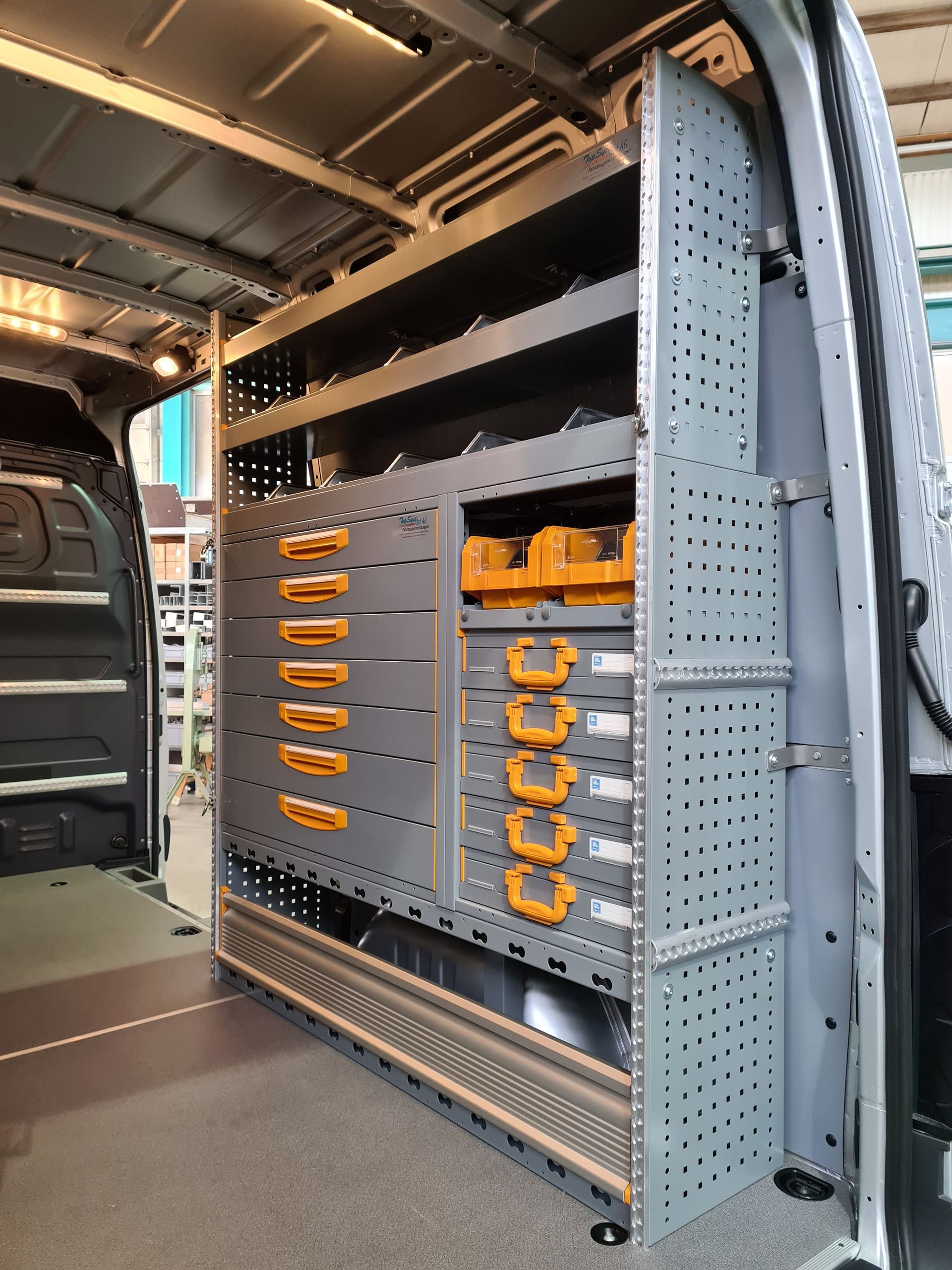 Innenausstattung des Lieferwagens mit maßgefertigten grauen Regalen und Schubladen zur Werkzeugorganisation.