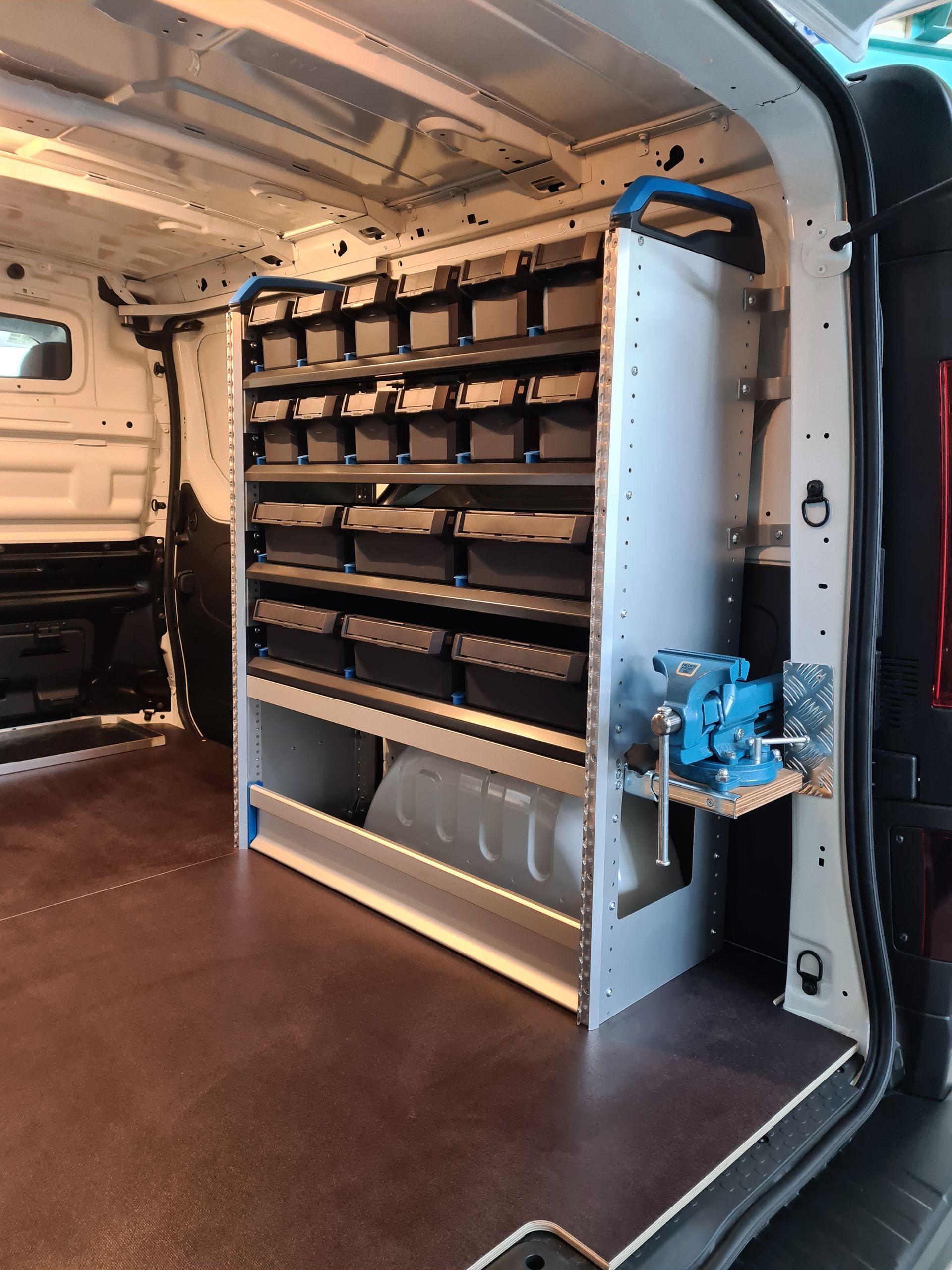 Innenansicht des Lieferwagens mit Regalen, Behältern und einem montierten blauen Schraubstock.
