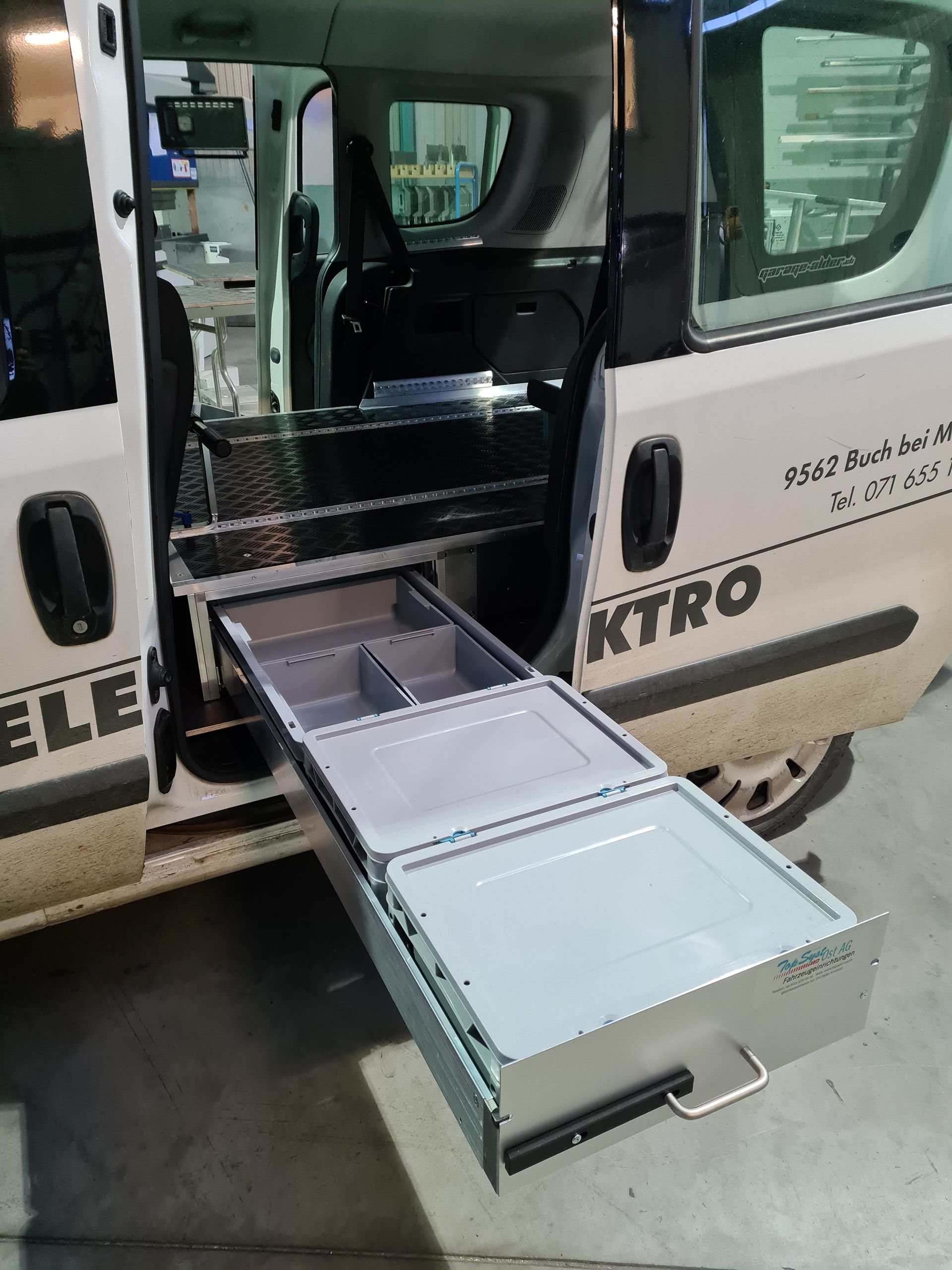 Weißer Lieferwagen mit offener Seitentür, hinter der sich ein ausziehbares Schubladensystem zur Aufbewahrung befindet.