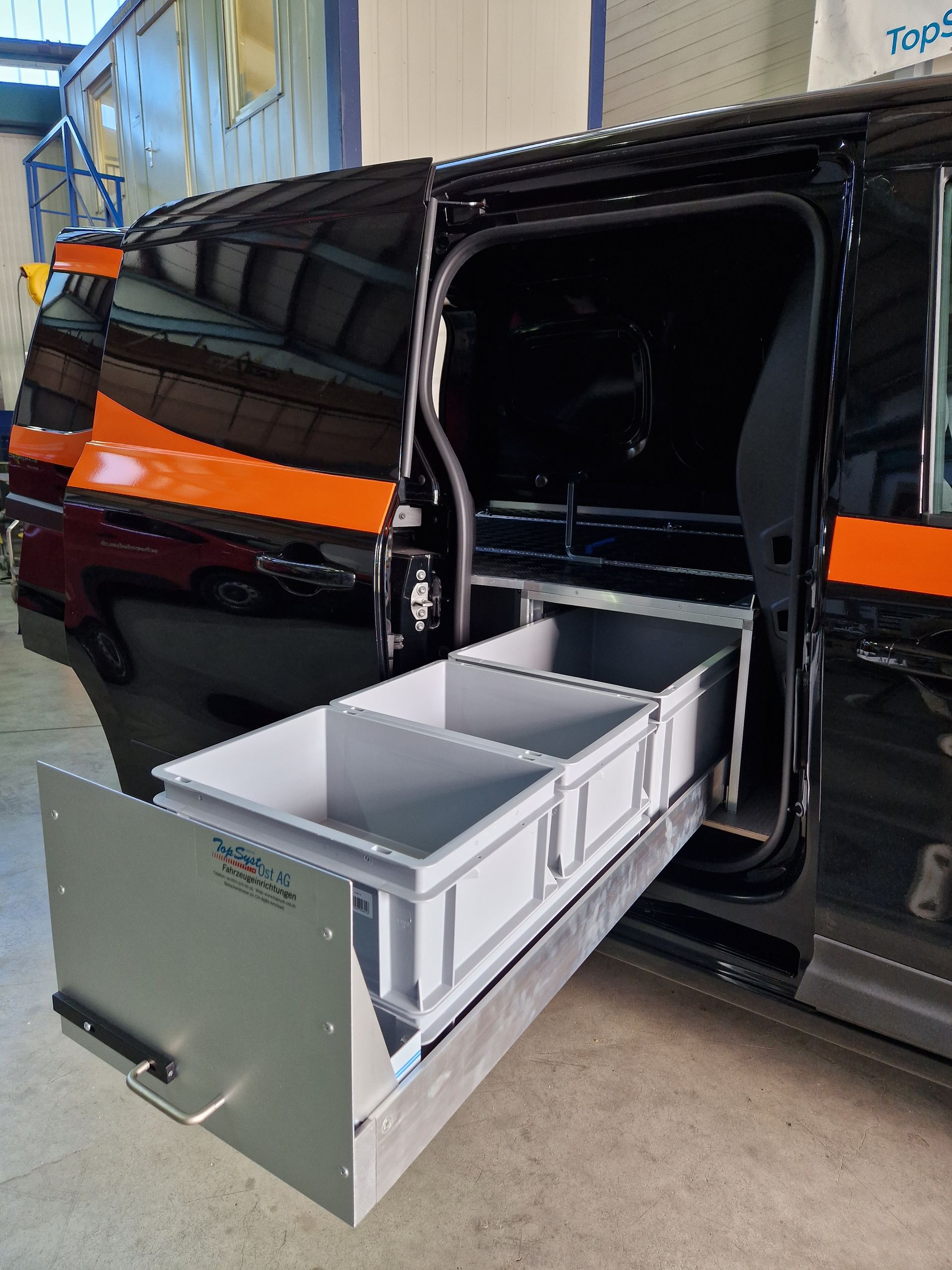 Schwarzer Lieferwagen mit offener Seitentür. Eine ausziehbare Schublade mit drei grauen Lagerfächern ist sichtbar.