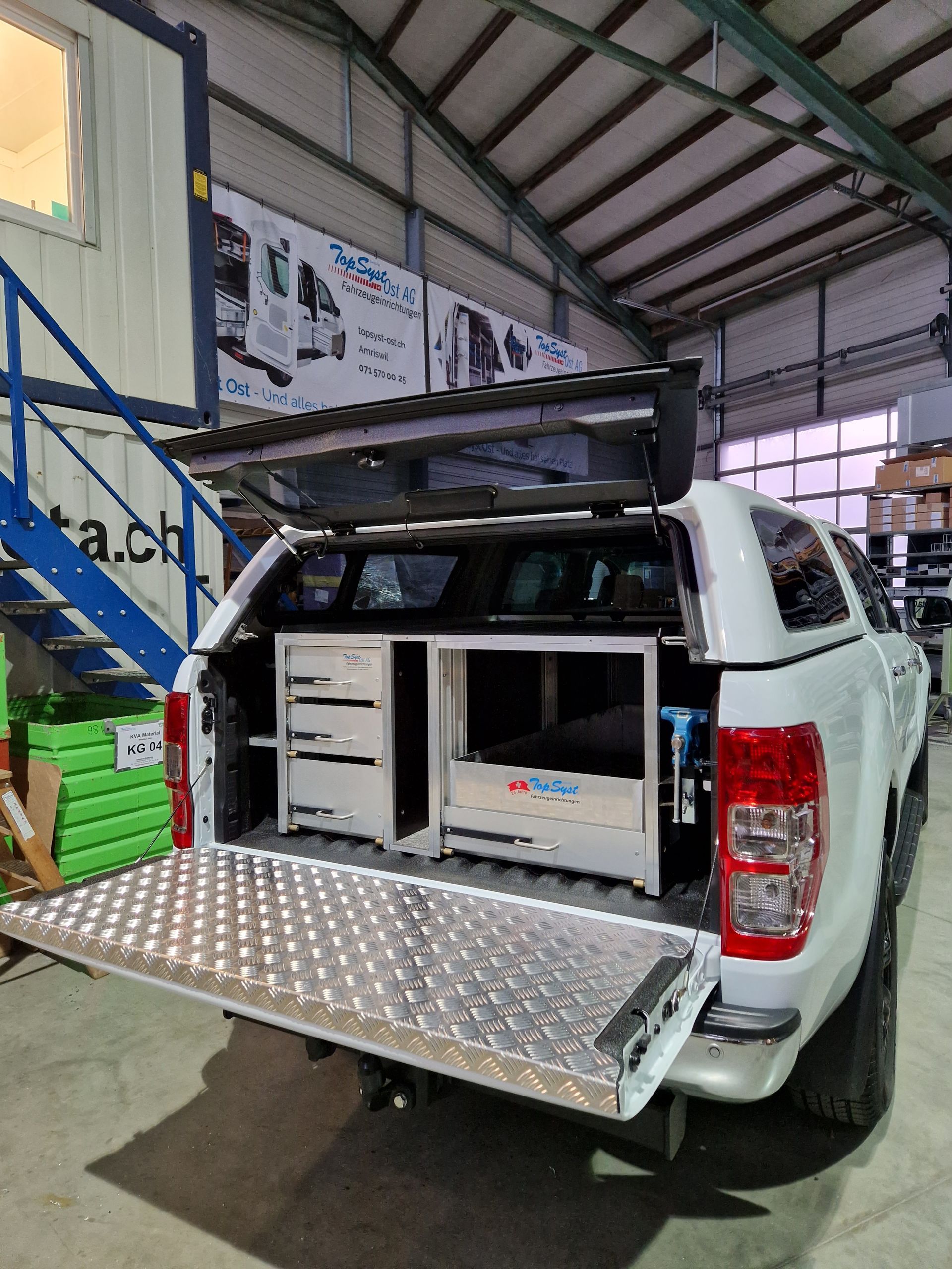 Weißer Pickup-Truck mit offener Heckklappe, die auf der Ladefläche eine individuell eingerichtete Werkstatt zum Vorschein bringt.