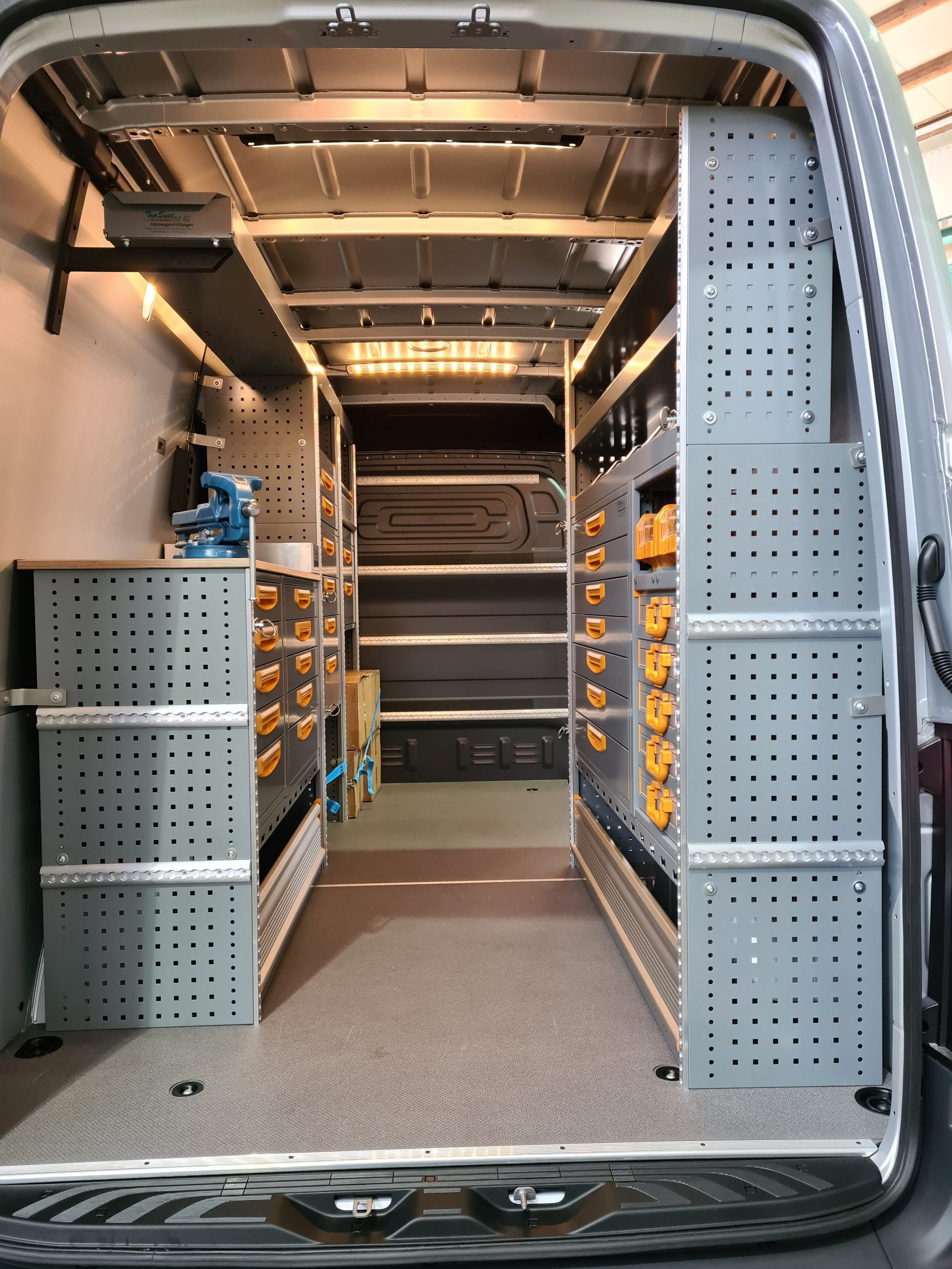 Innenraum eines Lieferwagens mit geordneten Regalen für Werkzeuge und Ausrüstung. Graue Metallregale säumen die Wände.