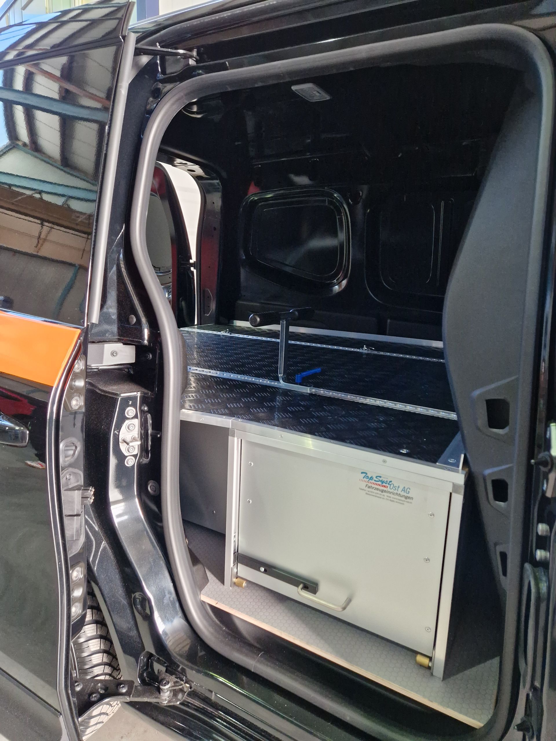 Schwarzer Van-Innenraum mit Einbauschränken und offener Tür.