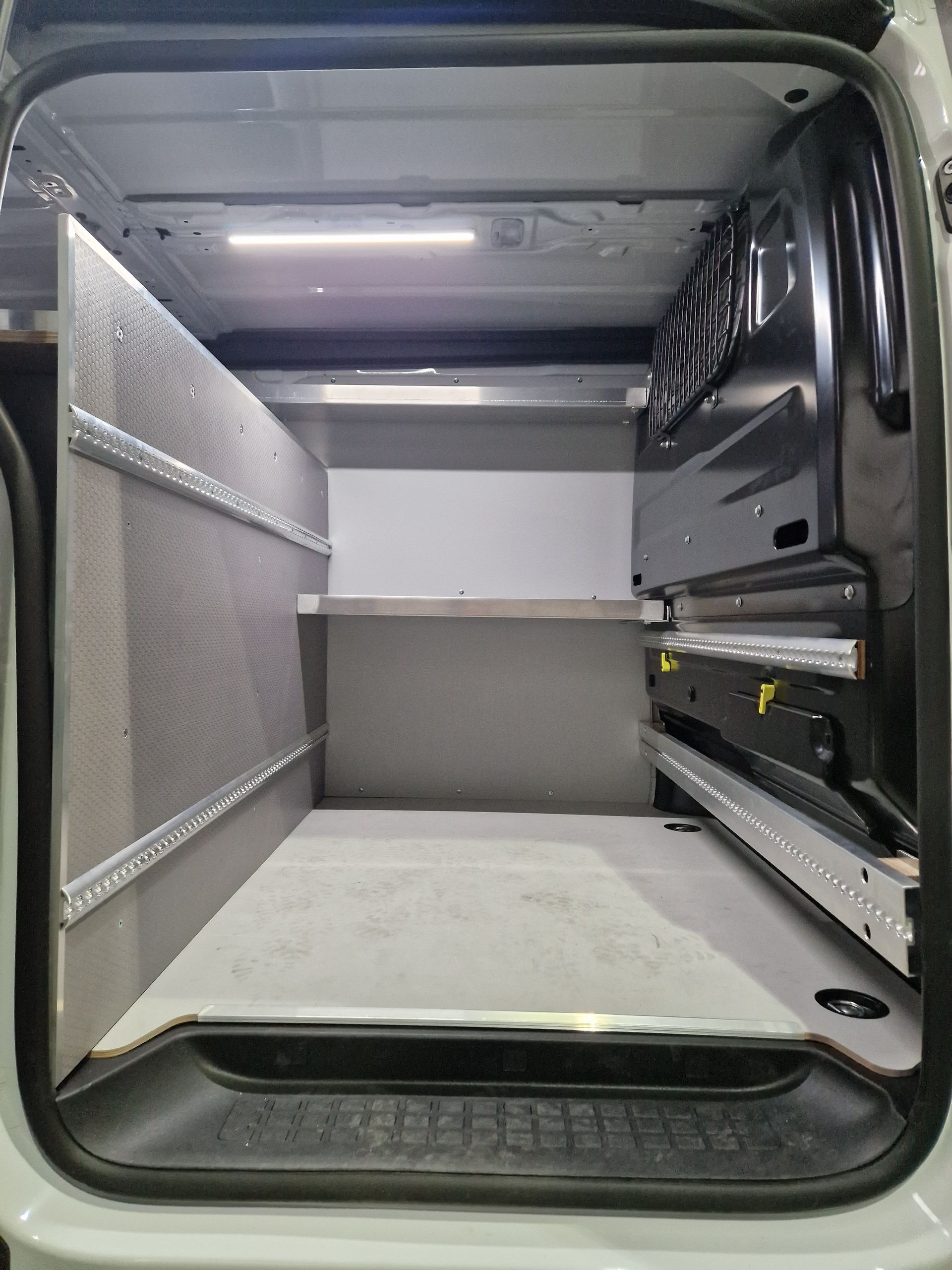 Innenansicht eines Lieferwagens mit Regalen. Graue und weiße Oberflächen, Deckenlicht.