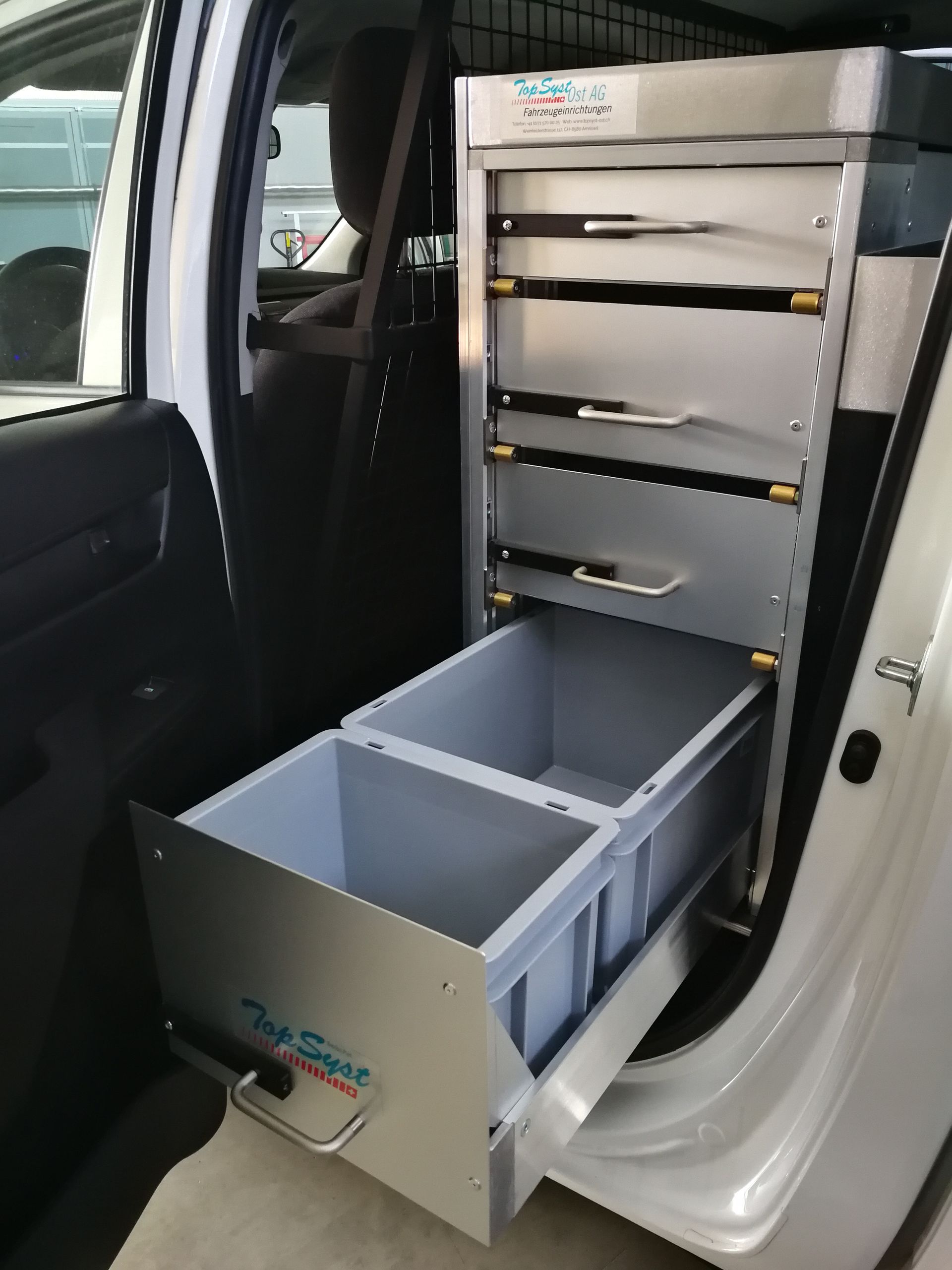 Schubladeneinheit mit Werkzeugen und Aufbewahrungsbehältern, eingebaut im Türrahmen eines weißen Fahrzeugs.