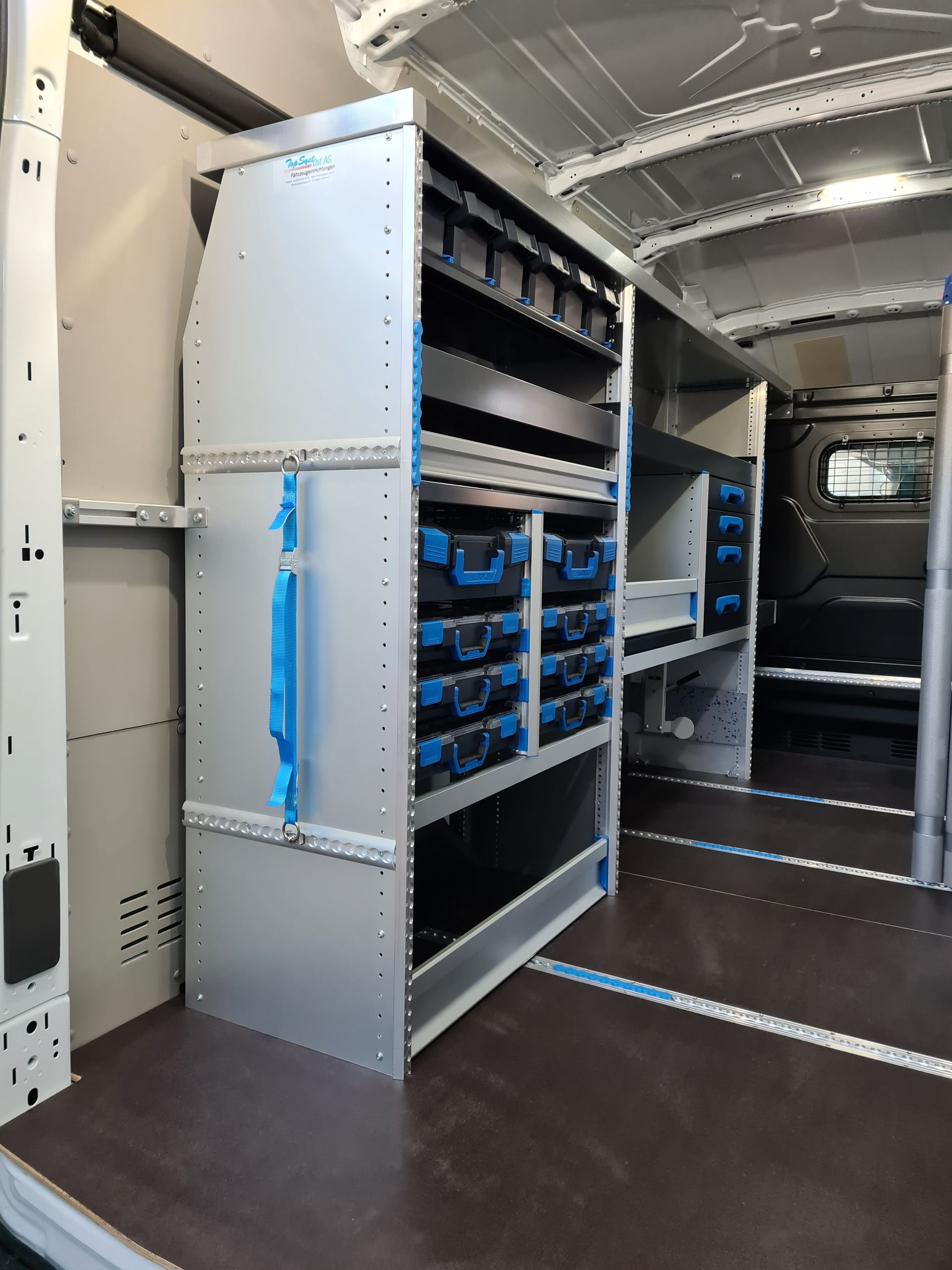 Innenraum eines Lieferwagens mit geordneten Regalen, Schubladen und Lagerbehältern in Grau und Blau.