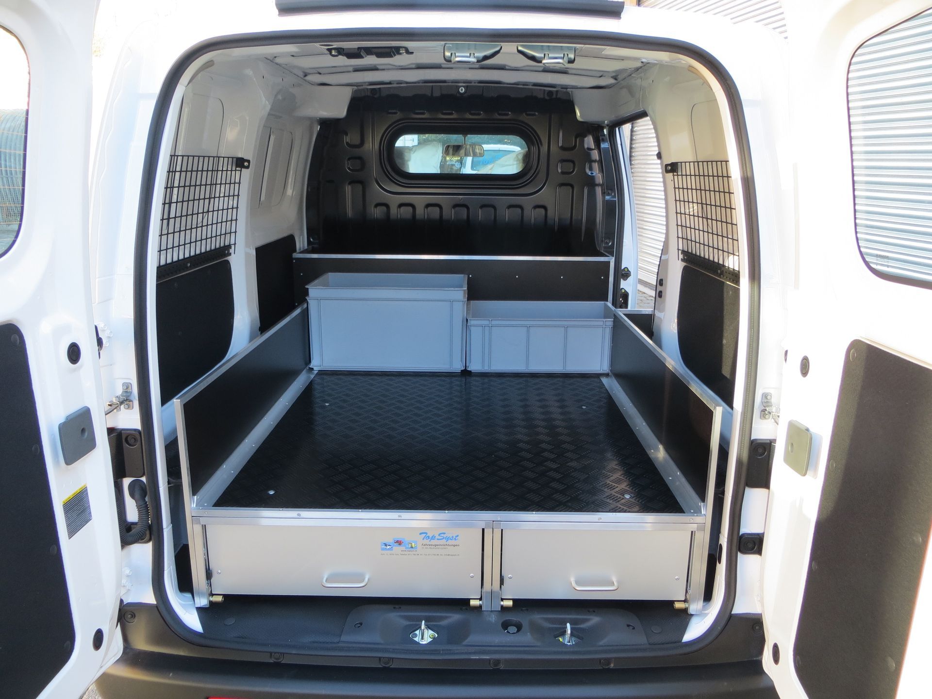 Weißer Lieferwageninnenraum mit schwarzem Bodenbelag, Aluminiumschubladen und Aufbewahrungsboxen.