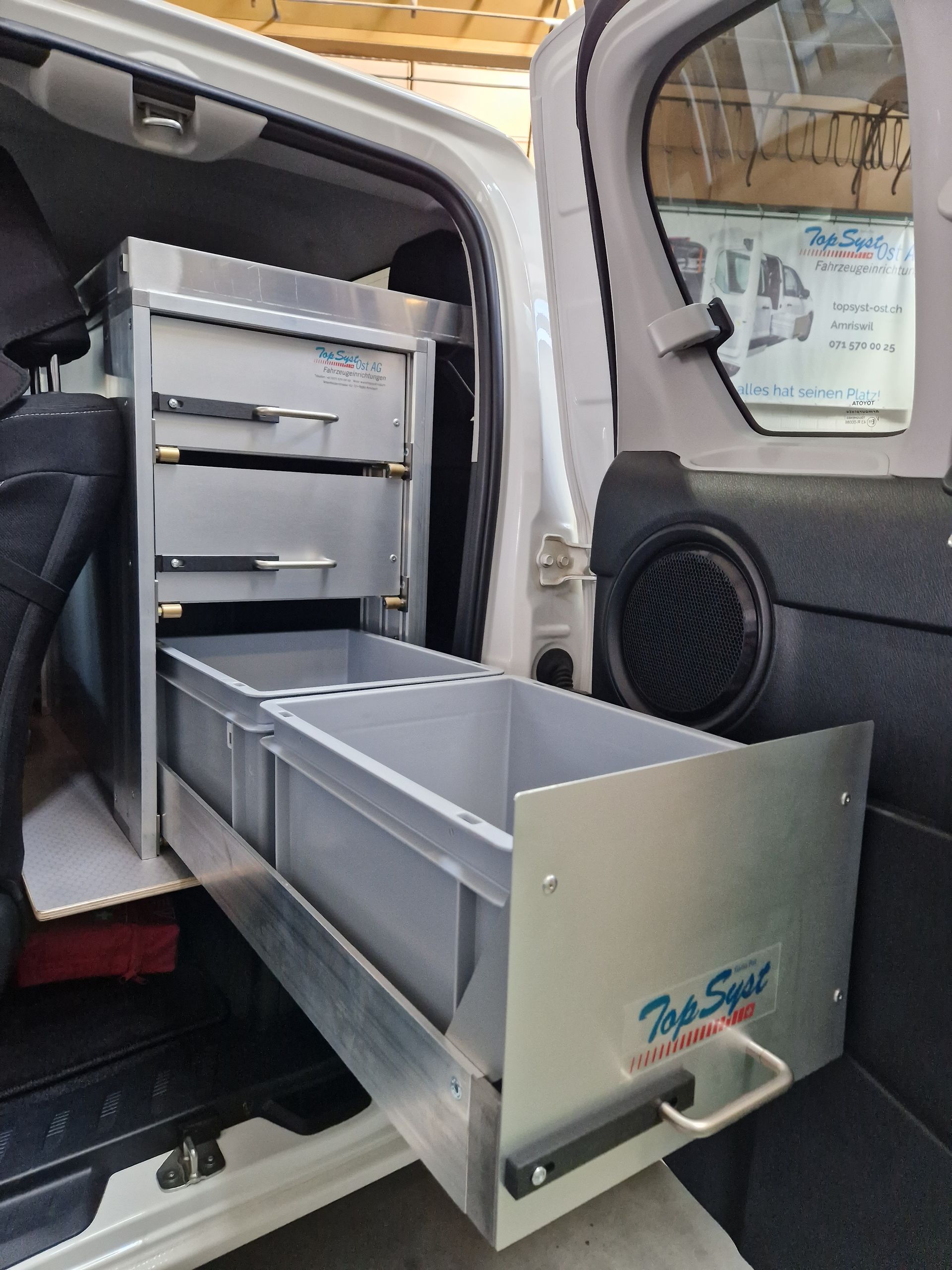 Silberne Metallschubladen in einem weißen Lieferwagen. Die Schubladen sind mit „Top Spirit“ beschriftet.