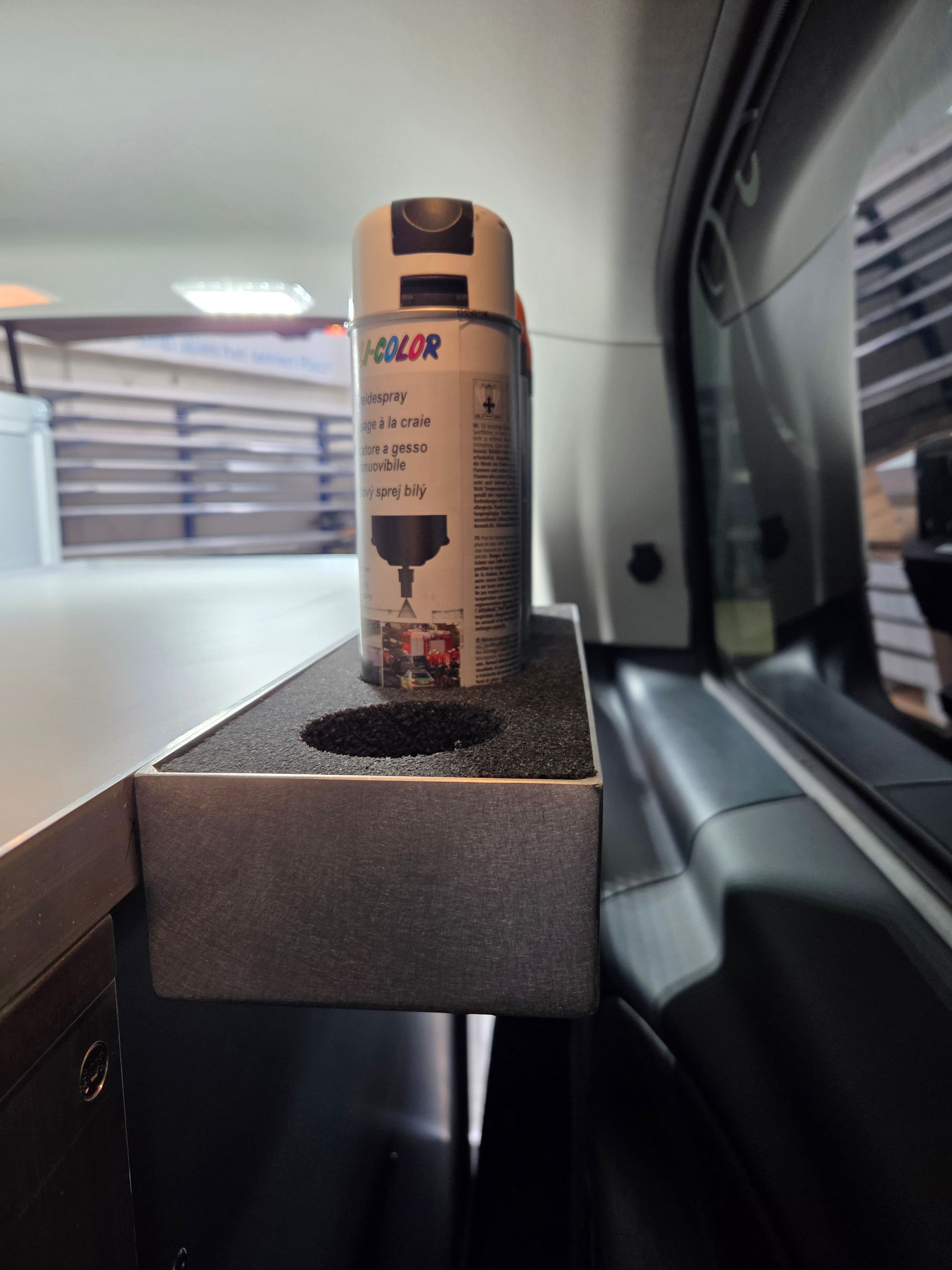 Sprühdose in einem speziellen Halter, in einem Fahrzeug, in der Nähe eines Fensters.