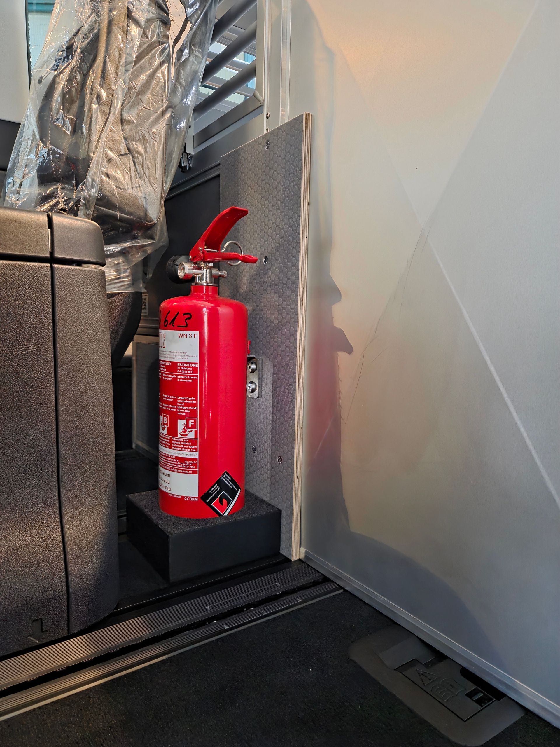 Roter Feuerlöscher auf schwarzem Sockel, in einem Fahrzeug.