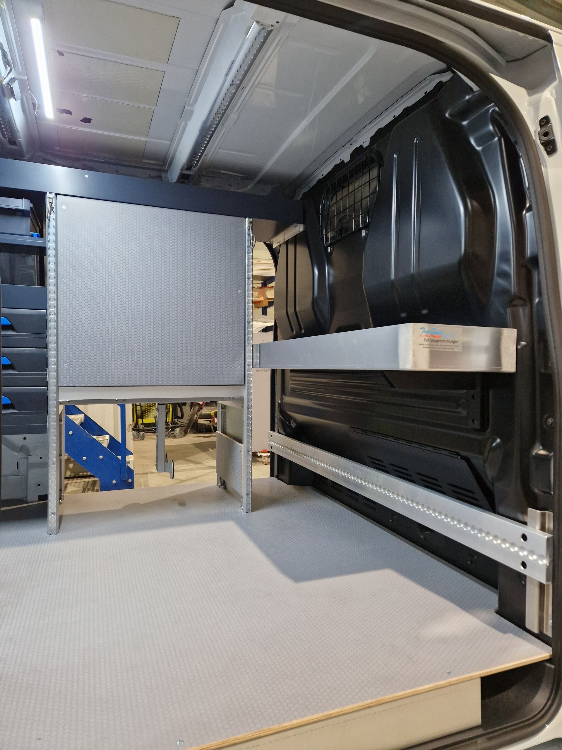 Innenraum eines Lieferwagens mit maßgefertigten Regalen und Arbeitsbereich. Graue und silberne Konstruktion.