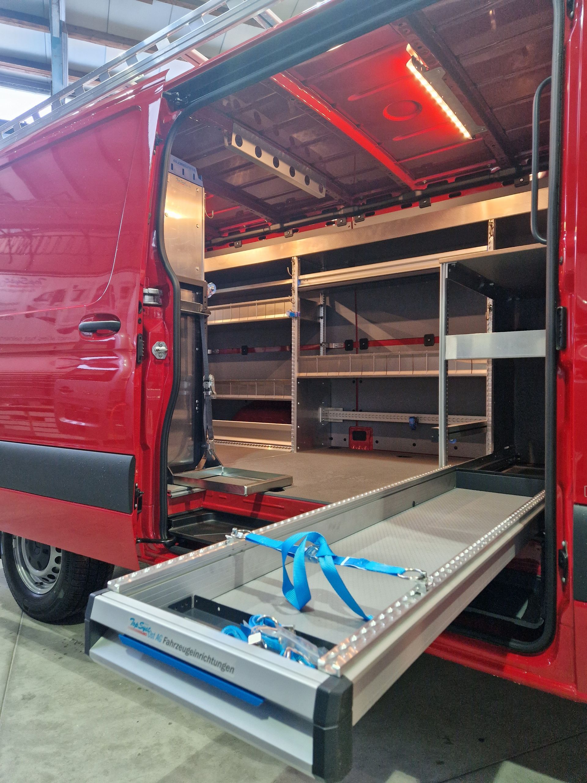 Roter Lieferwagen mit offener Seite und ausgefahrener Ladefläche. Innenregale und rote LED-Beleuchtung sichtbar.